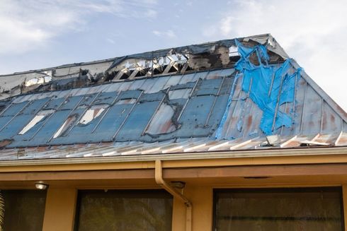 Damaged blue metal roof with torn tarp and debris on a building