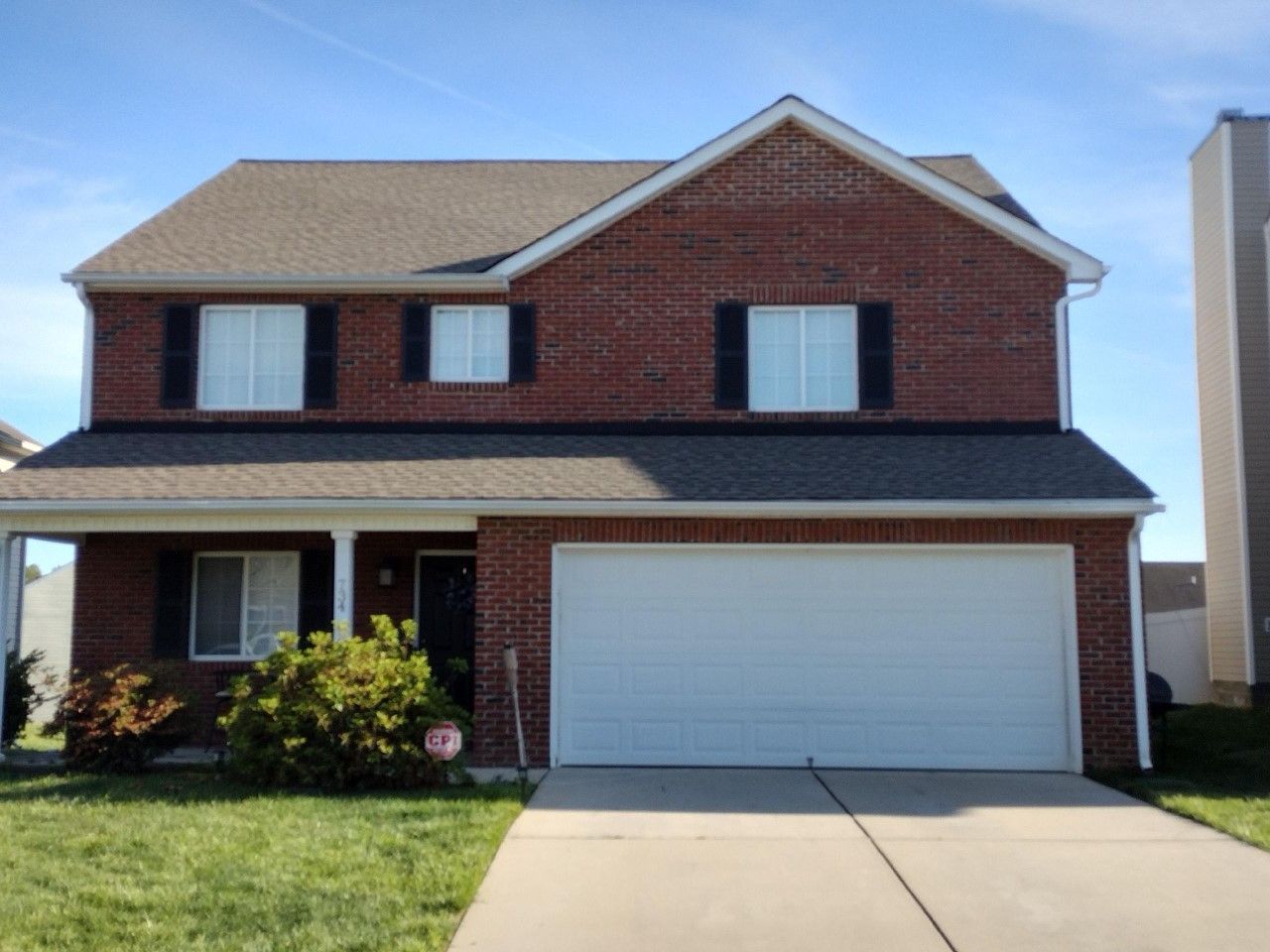 Two-story brick house with white garage and front porch under a clear blue sky