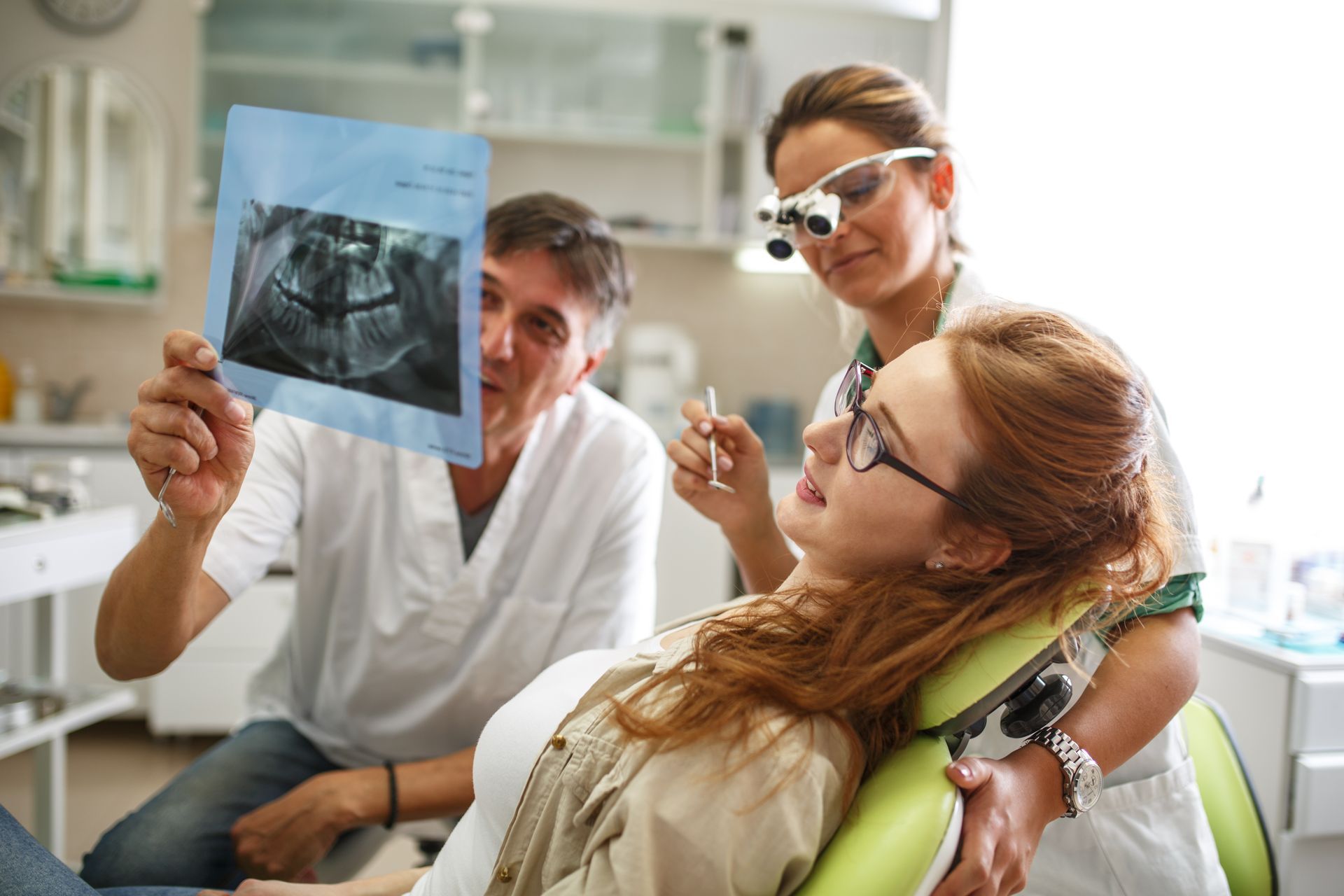 a woman is sitting in a dental chair looking at an x-ray of her teeth.