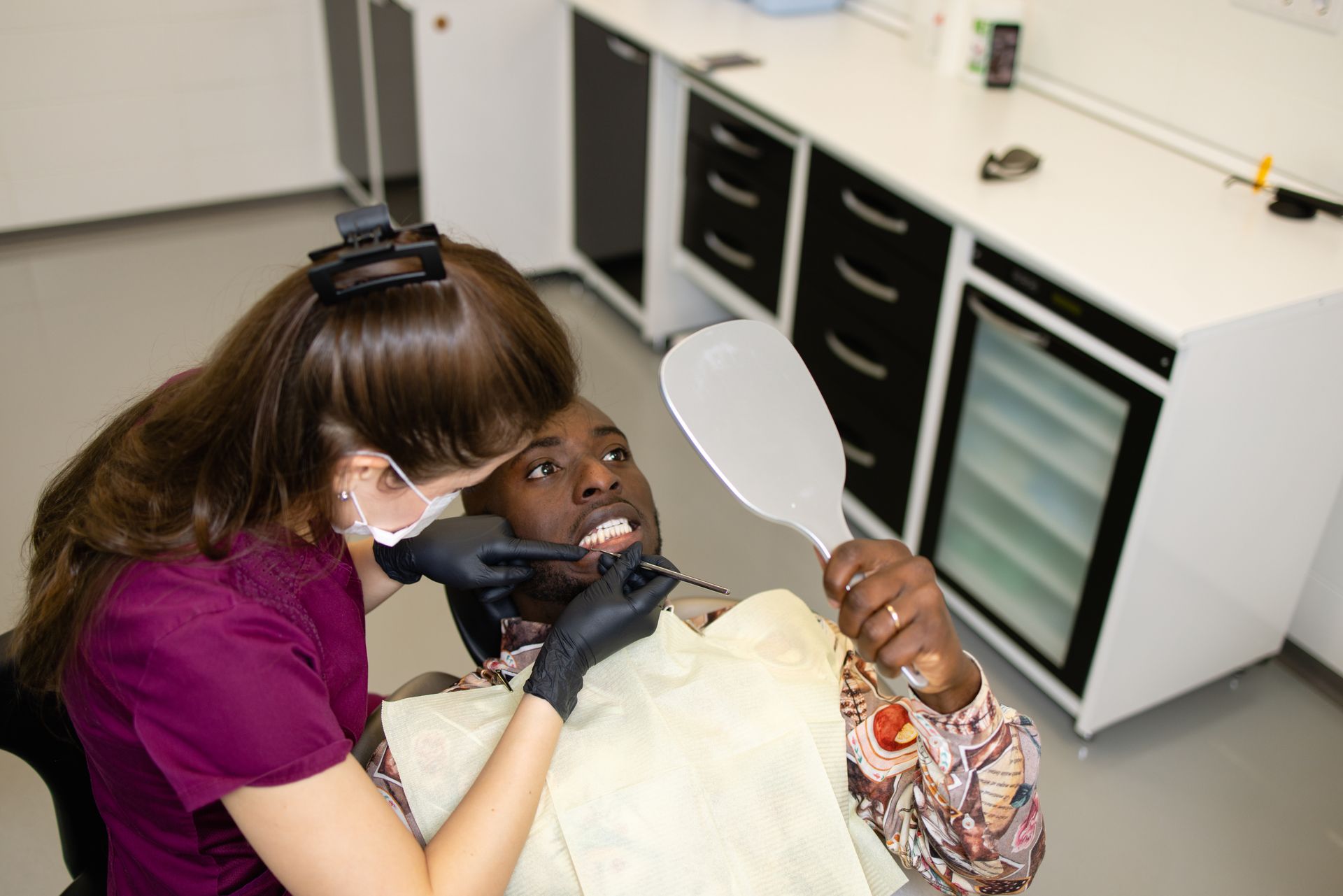 a woman is examining a man 's teeth in the San Diego dental office.