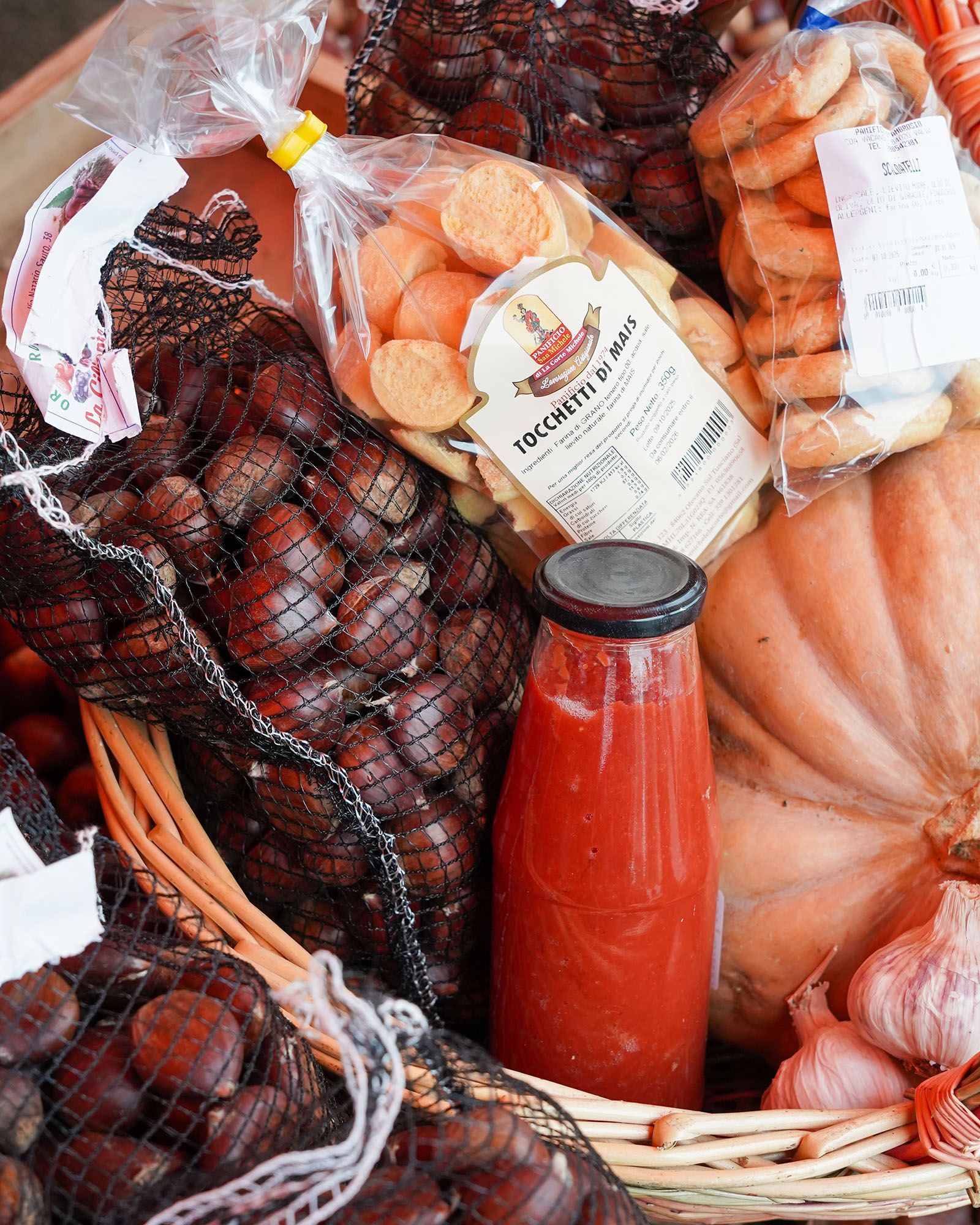 Castagne in sacchetti di rete, biscotti, salsa di pomodoro, aglio e zucca in un cestino.