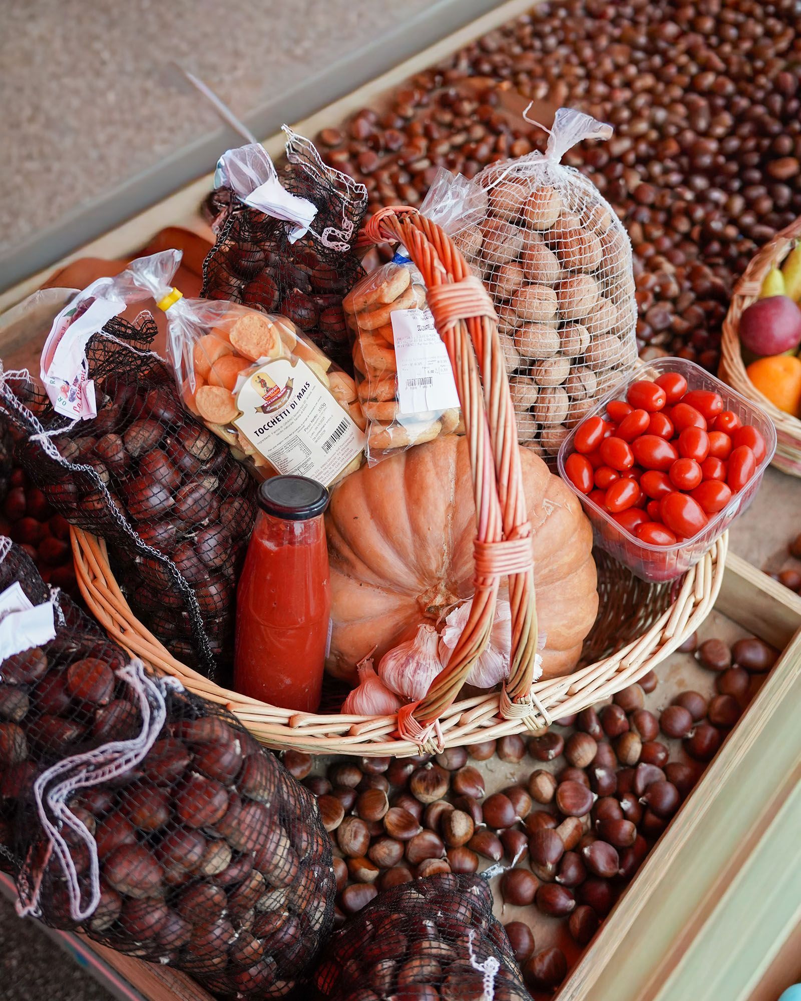 Un cesto di prodotti autunnali: castagne, zucca, pomodori, aglio, biscotti e salsa.