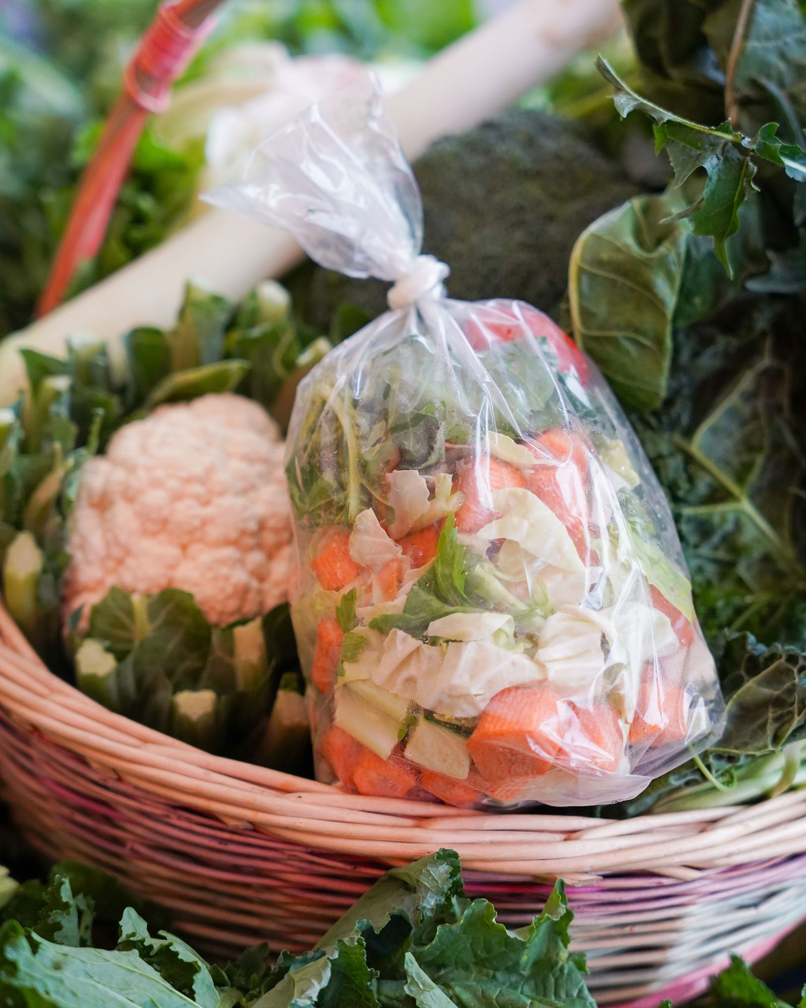Cesto di verdure, tra cui cavolfiore, porro e un sacchetto di plastica con carote, sedano e verdure a foglia tritate.