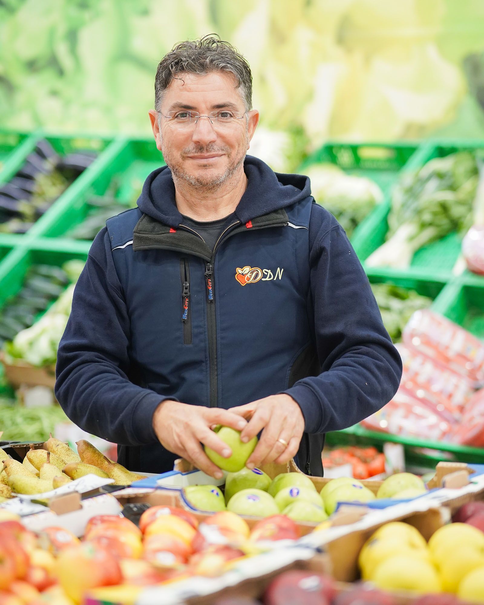 Uomo in giacca blu che tiene in mano una mela verde in una bancarella di frutta.
