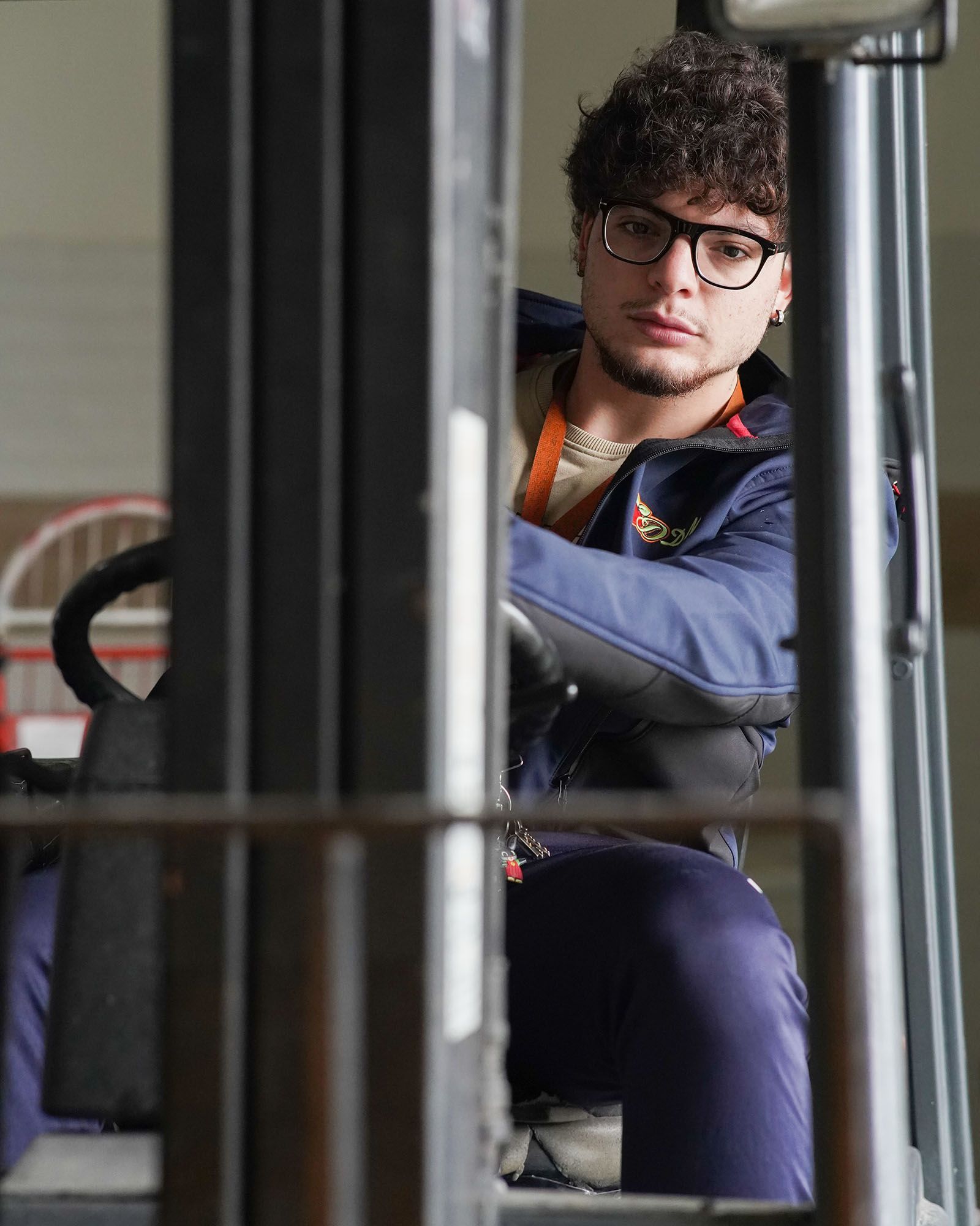 Uomo alla guida di un carrello elevatore, con occhiali e uniforme blu.