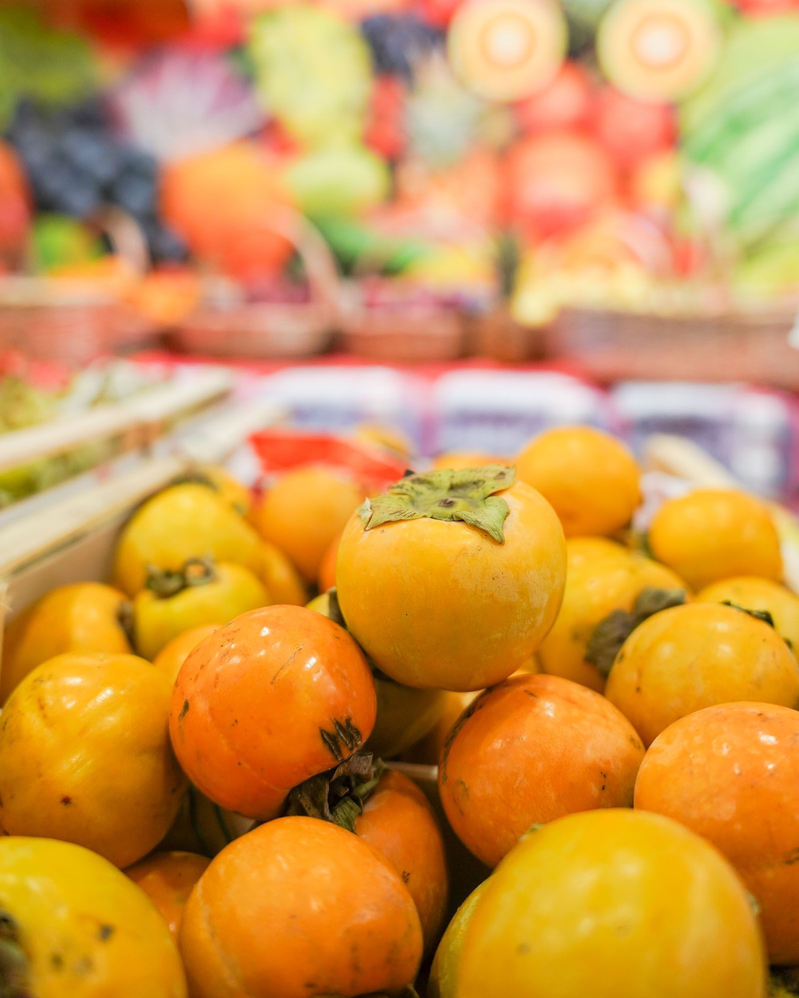 Mucchio di cachi arancioni e gialli in una cassa di legno, con frutti sfocati sullo sfondo.