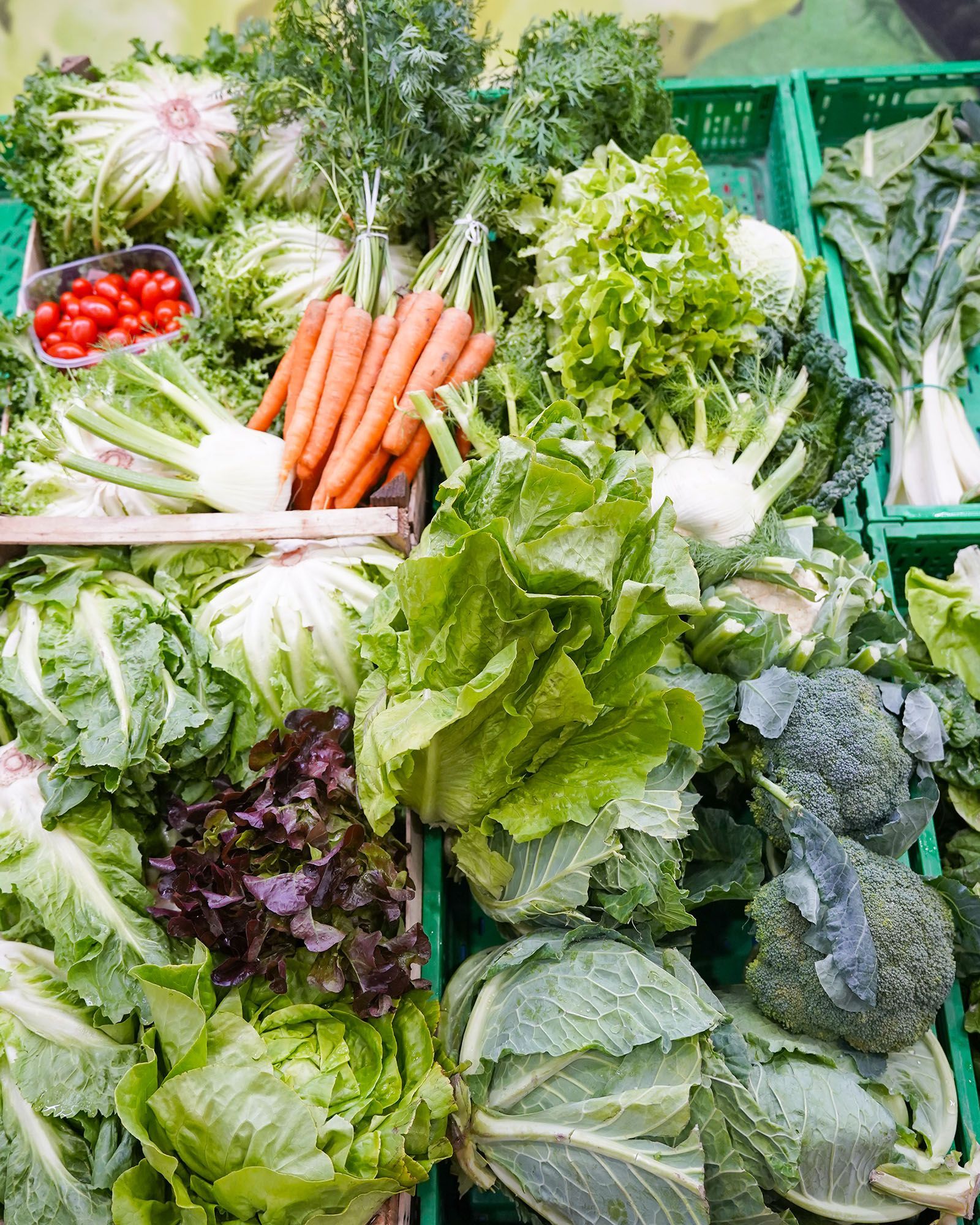 Verdure in contenitori verdi: carote, lattuga, broccoli, pomodori e altro ancora al mercato.