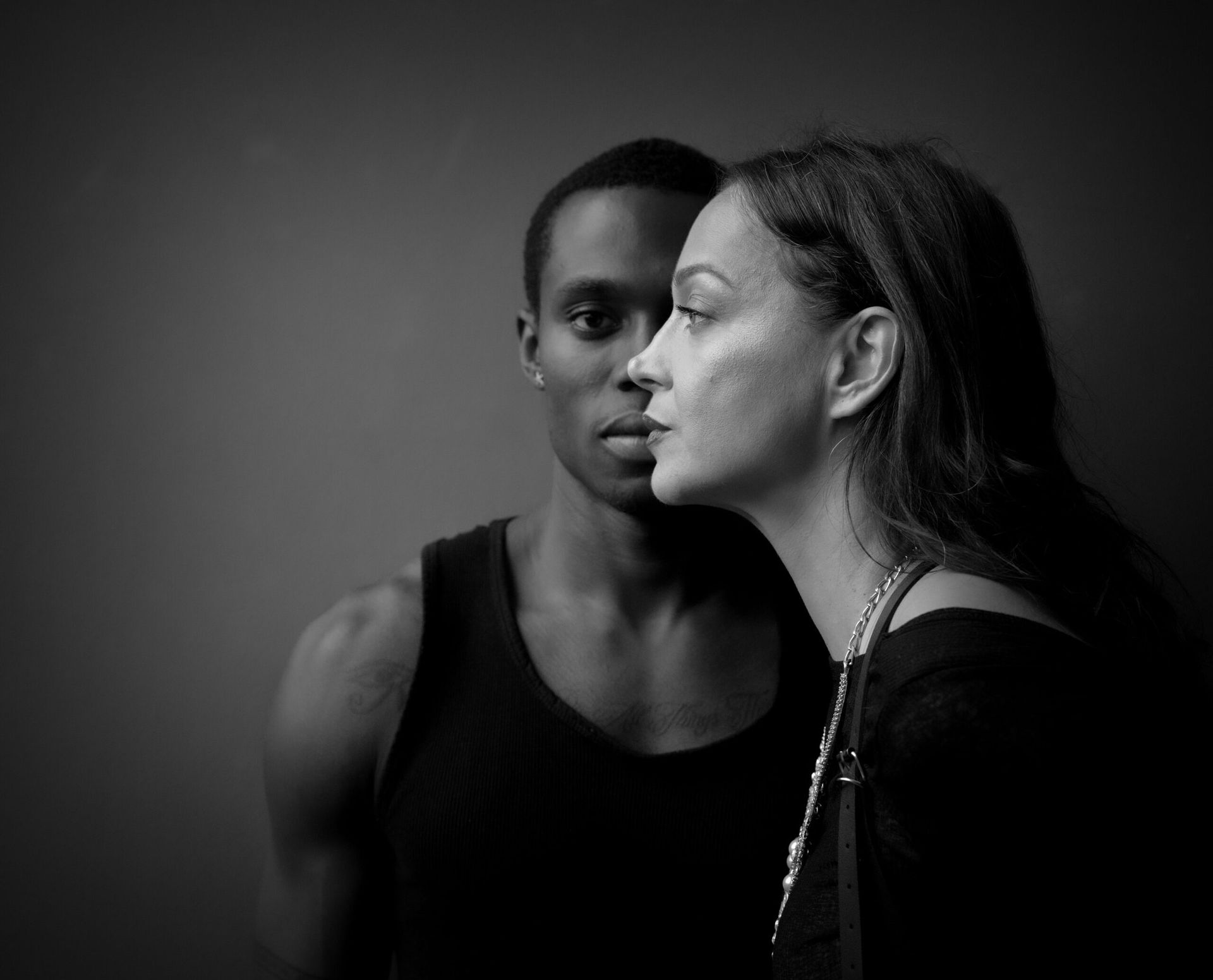 Photo en noir et blanc d'un homme et d'une femme. La femme se penche vers lui ; ils partagent le même espace. Fond sombre.
