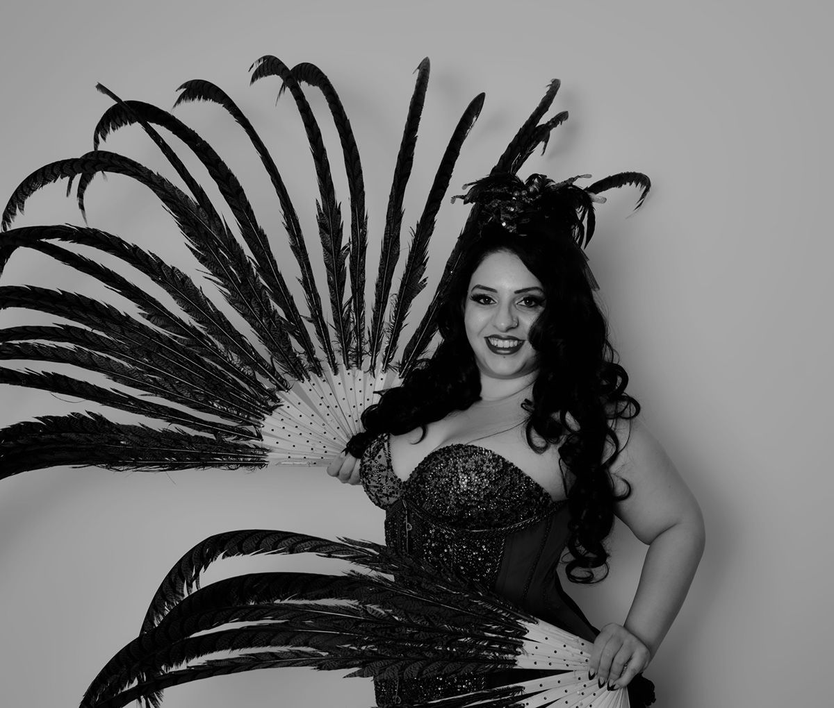 Une femme en costume à plumes sourit, tenant de grands éventails noirs et blancs.