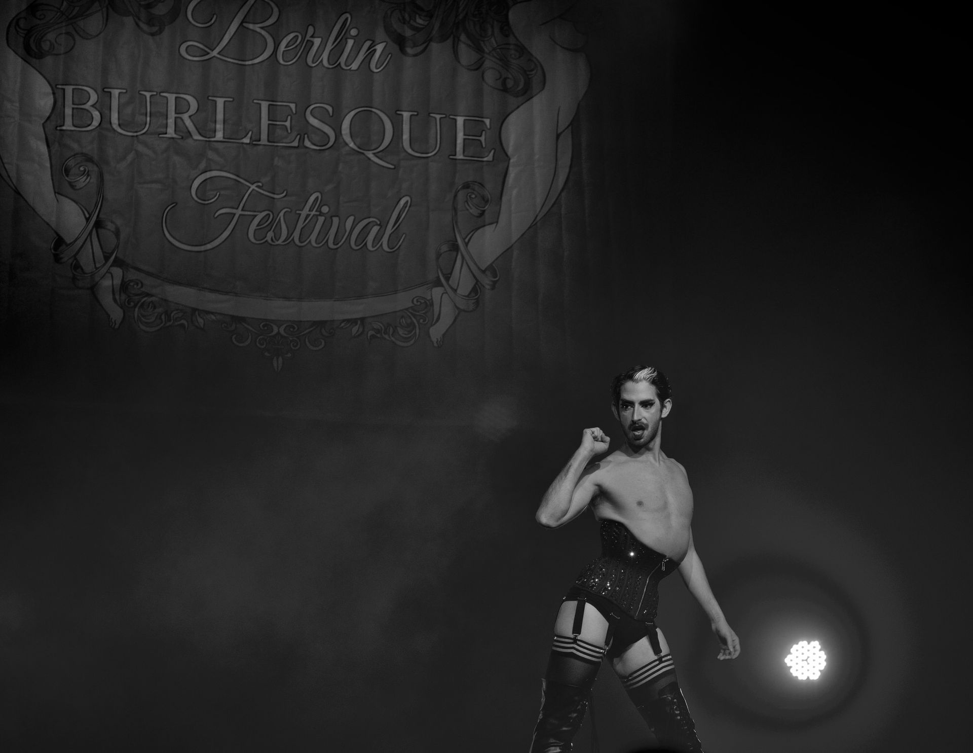Une artiste de spectacle burlesque, vêtue d'un corset, d'un porte-jarretelles et de bas cuissardes, prend la pose sur scène.
