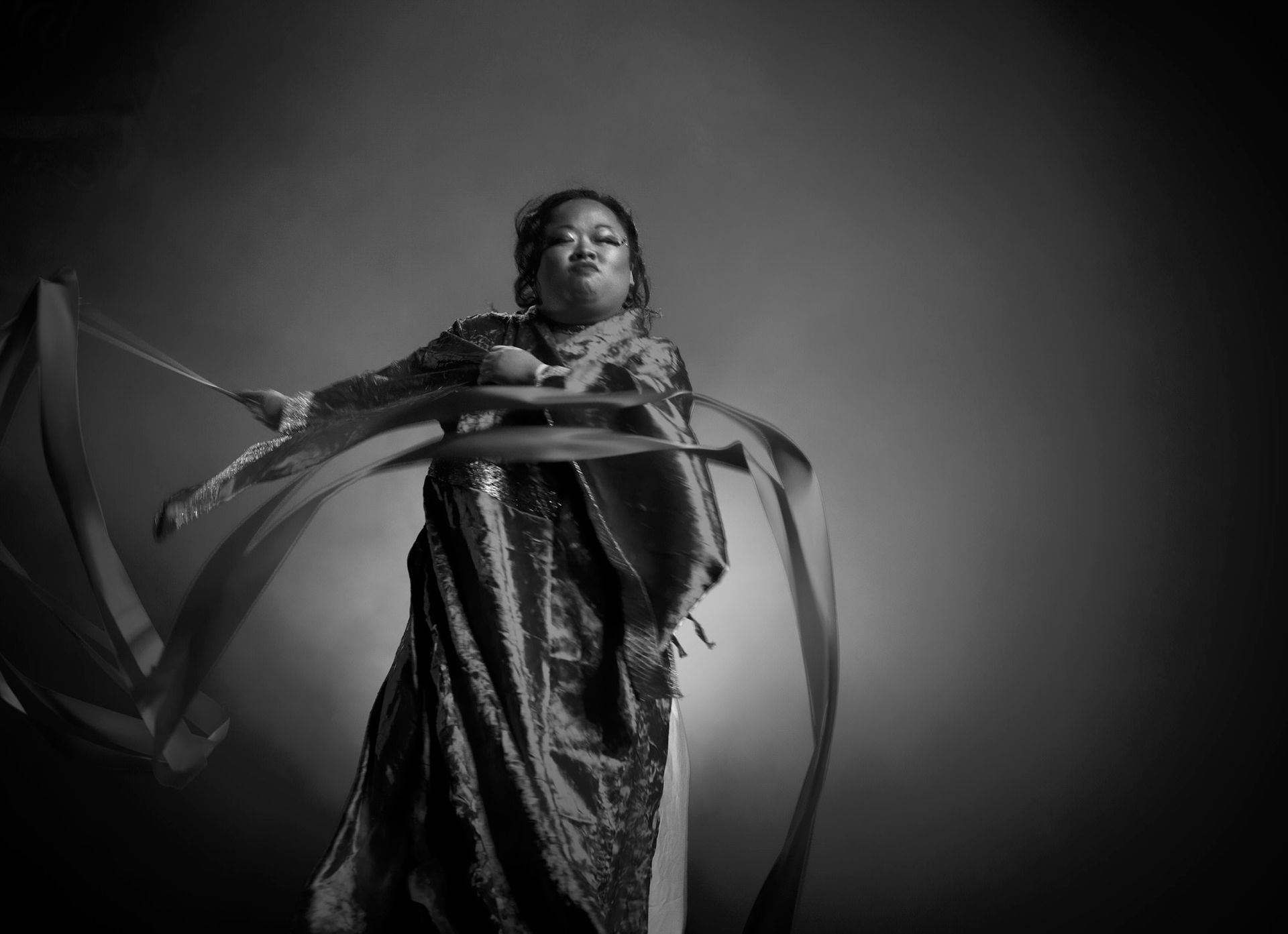 Femme en robe ornée faisant tournoyer des rubans, exécutant une danse sur fond sombre.