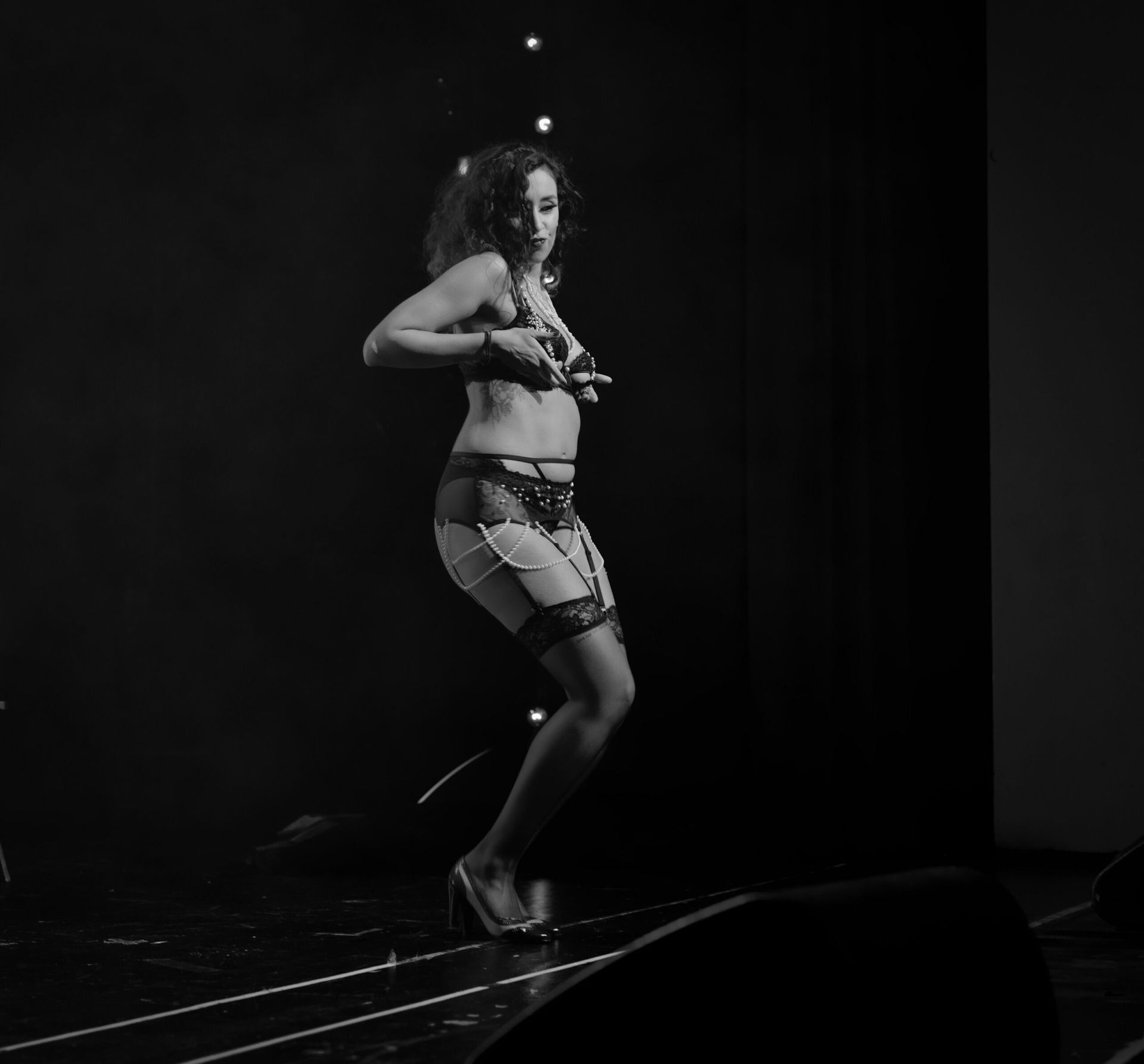 Femme en lingerie sur scène, ajustant son haut. Photo en noir et blanc.
