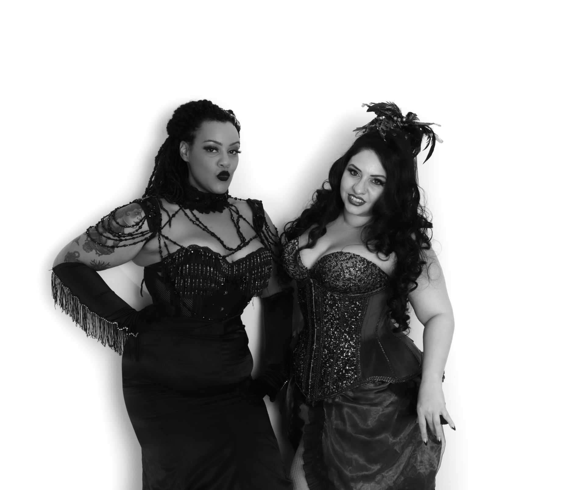 Deux femmes vêtues de tenues noires ornées posent devant un fond blanc.