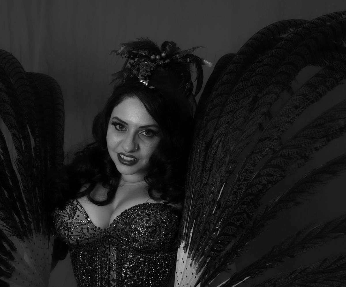Femme en corset à paillettes et ailes de plumes élaborées, regardant le spectateur.