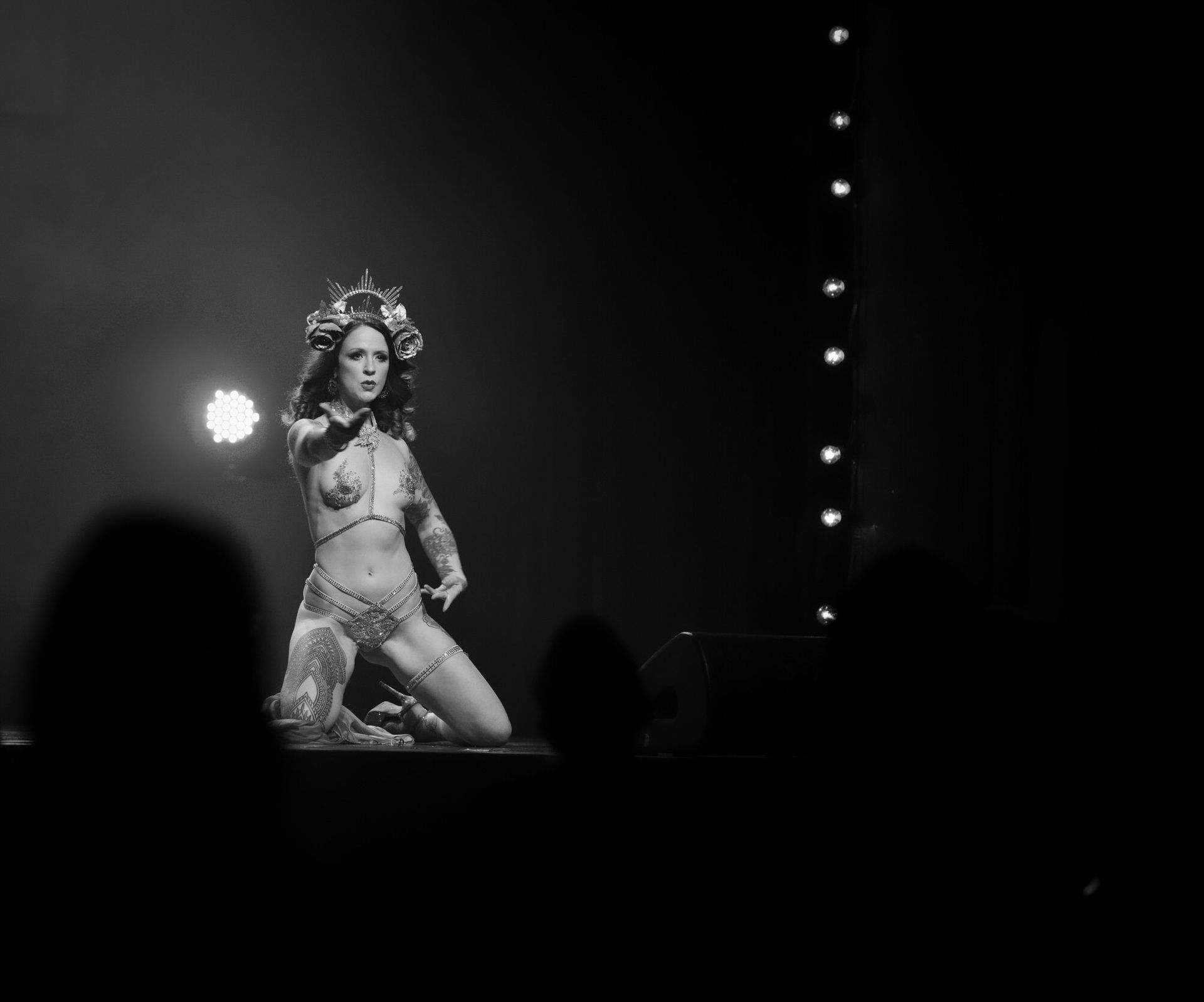 Une artiste burlesque s'agenouille sur scène en costume, tendant la main vers le public.