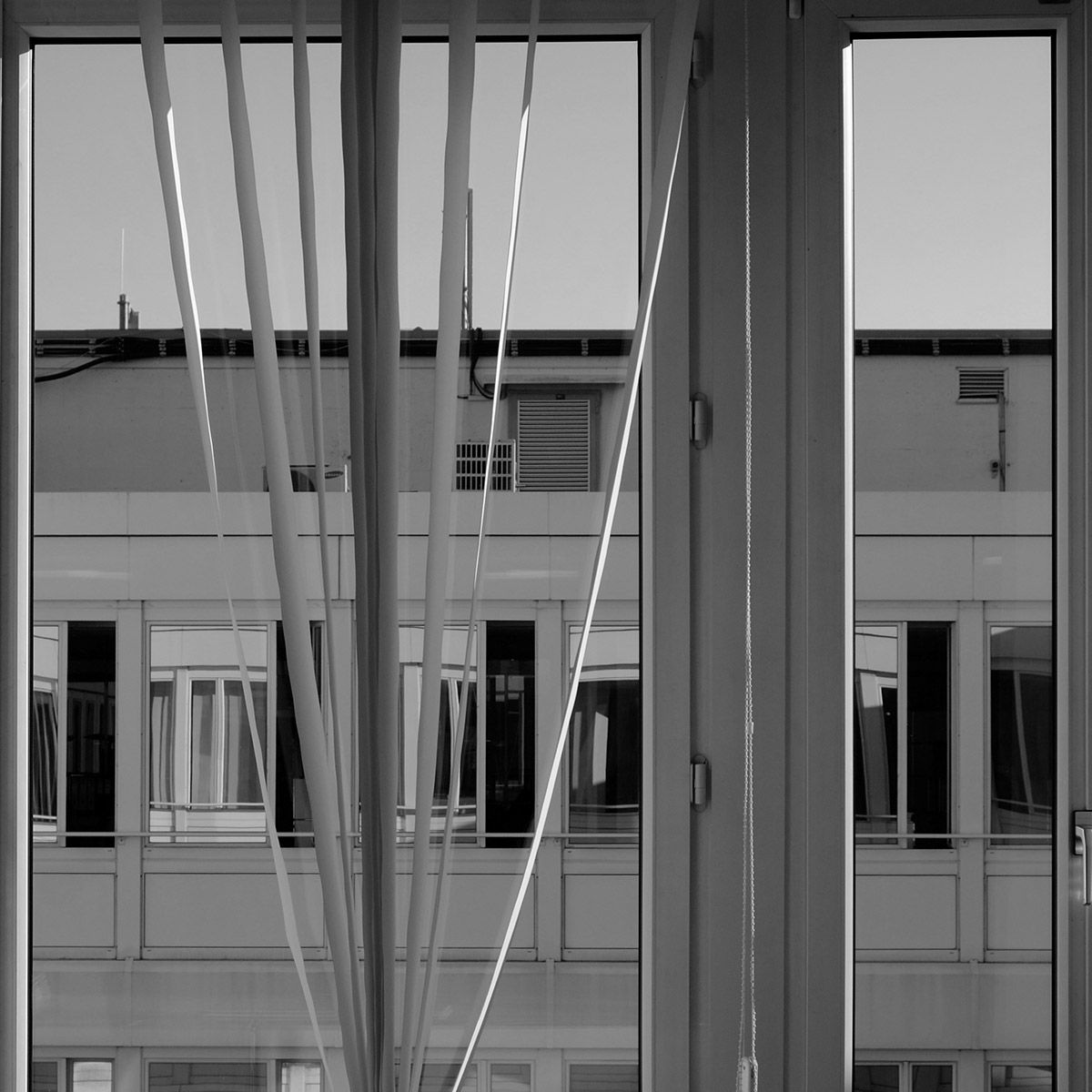 Fenêtre avec stores verticaux ; reflets des bâtiments visibles dans la vitre.