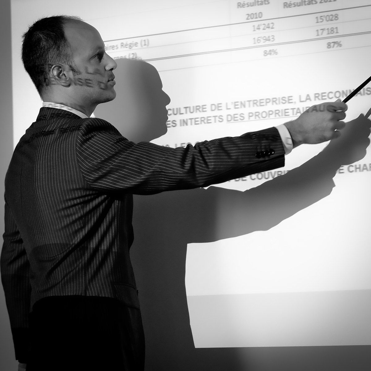 Un homme en costume désigne du doigt une présentation projetée à l'aide d'un stylo.