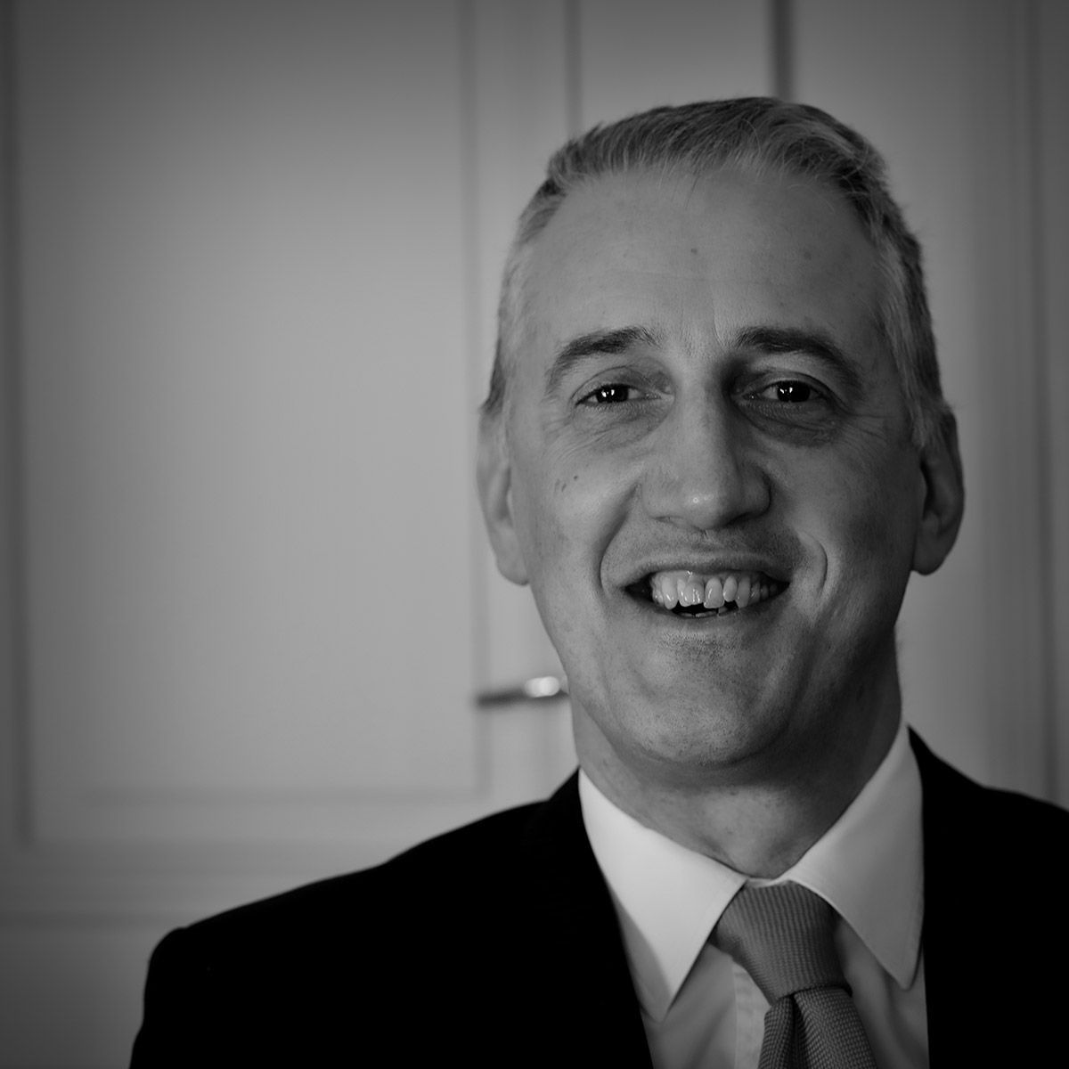 Un homme en costume sourit, à l'intérieur.