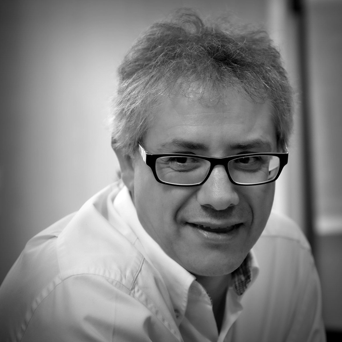 Un homme portant des lunettes sourit, en gros plan noir et blanc.