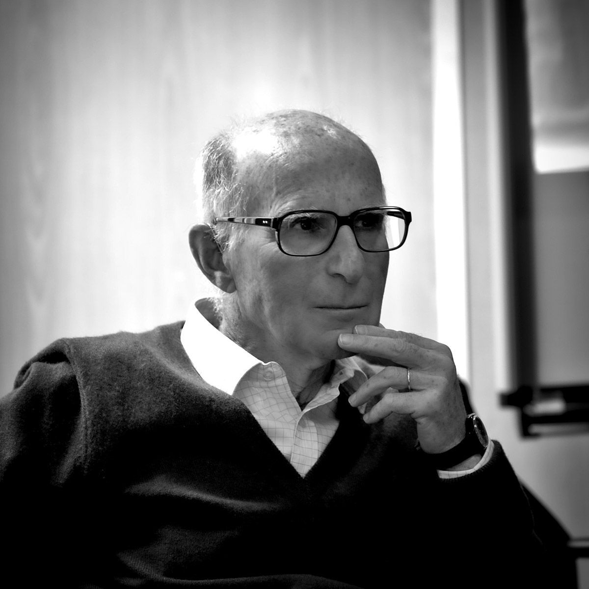 Un homme portant des lunettes et un pull, le menton appuyé sur la main, l'air pensif.