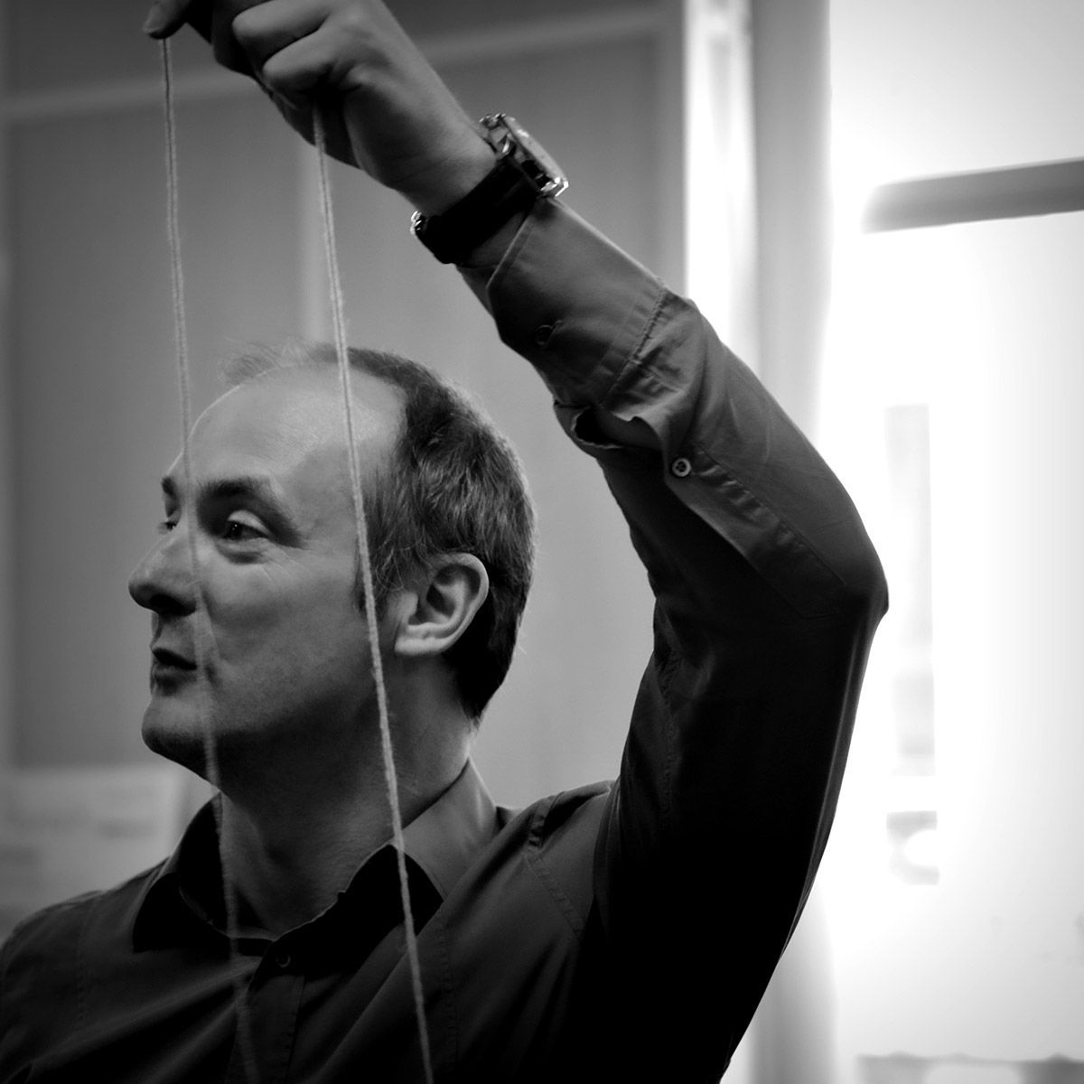Homme tenant des ficelles de la main droite, regardant vers le haut et la gauche. Photo en noir et blanc.