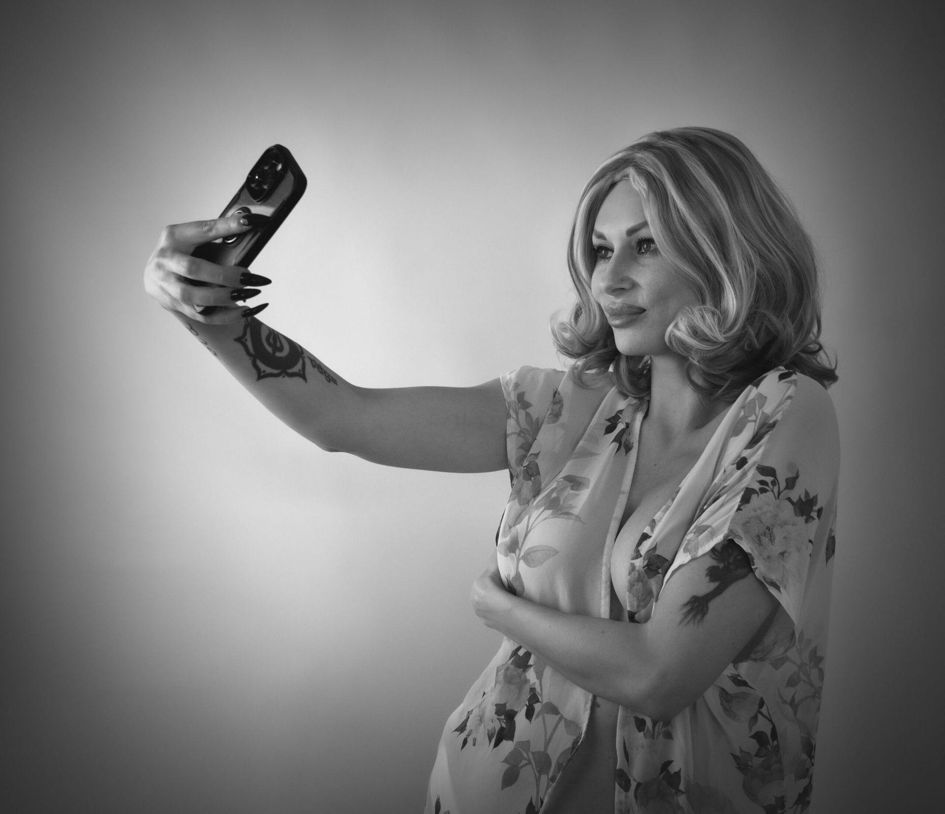 Une femme prend un selfie avec son téléphone, vêtue d'une robe à fleurs noire et blanche.