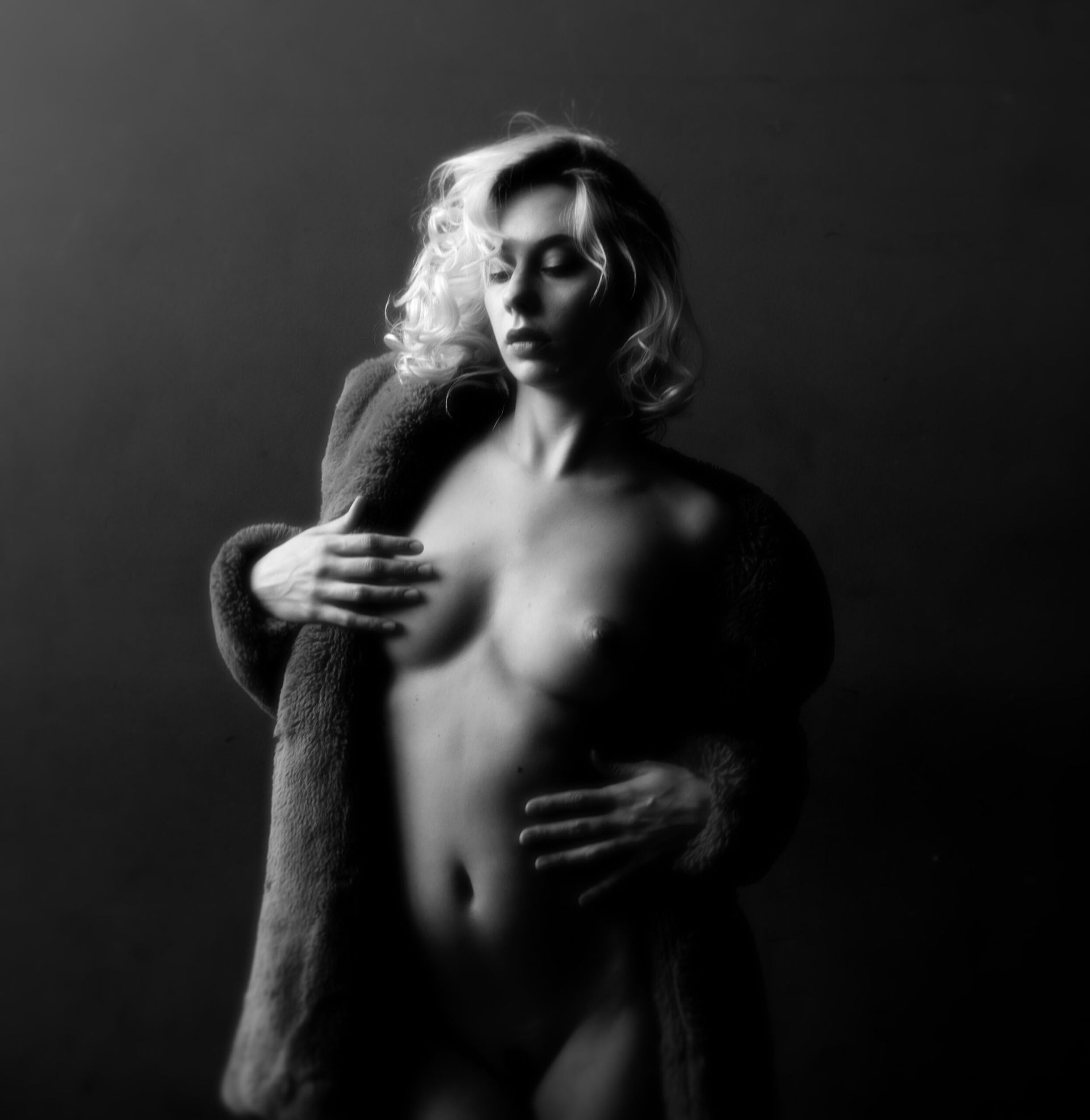 Femme nue en manteau de fourrure, se couvrant. Portrait en noir et blanc réalisé en studio.