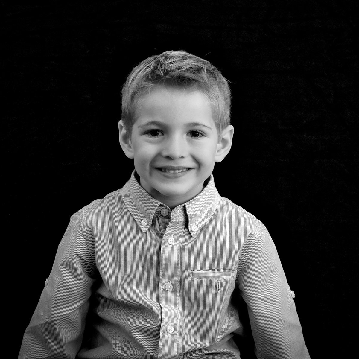 Enfant souriant portant une chemise rayée boutonnée sur fond noir.