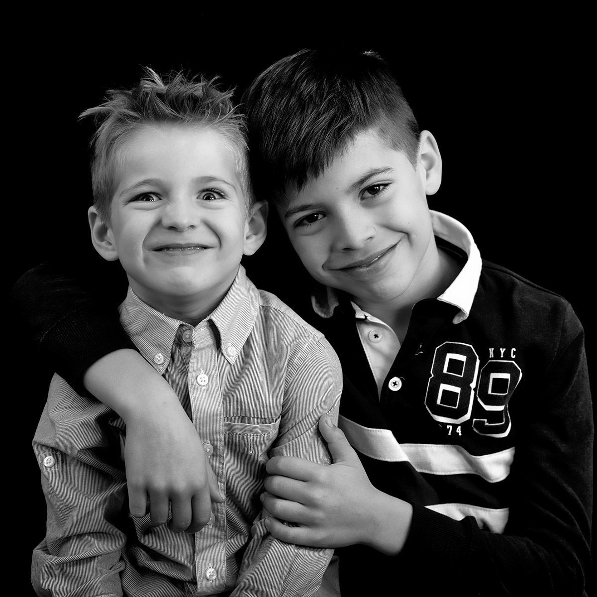 Deux garçons souriants posent côte à côte, l'un ayant un bras autour des épaules de l'autre. Photo en noir et blanc.