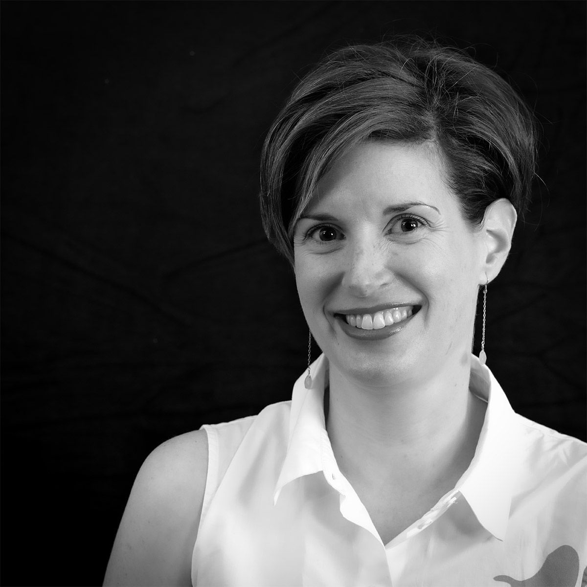 Femme souriante, vêtue d'un chemisier blanc sans manches, dans un portrait en noir et blanc.