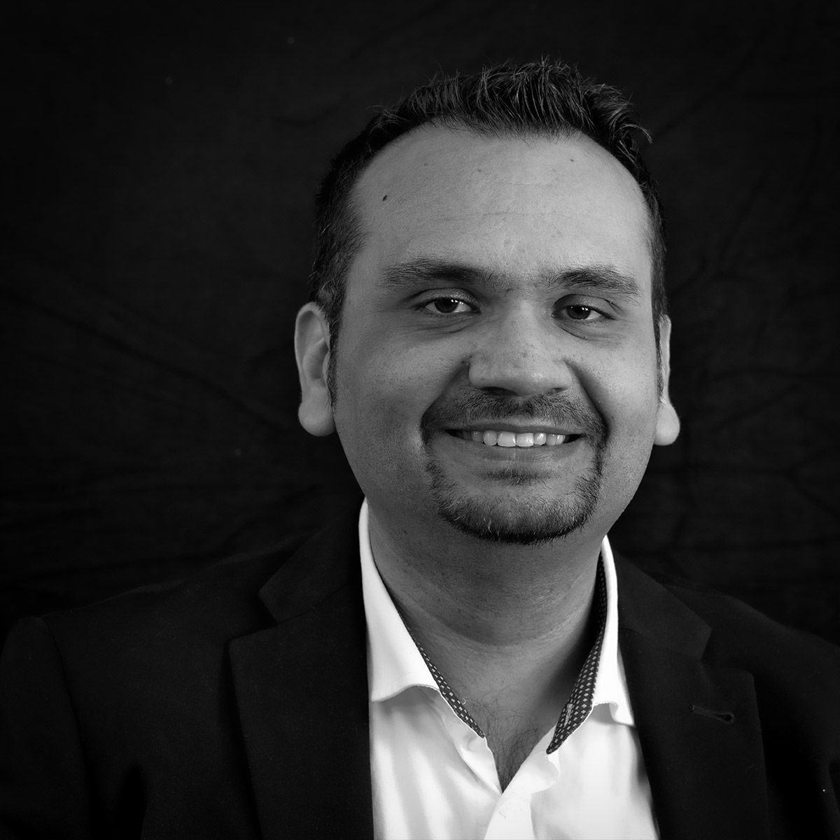 Un homme en blazer sourit à l'objectif, portrait en noir et blanc.