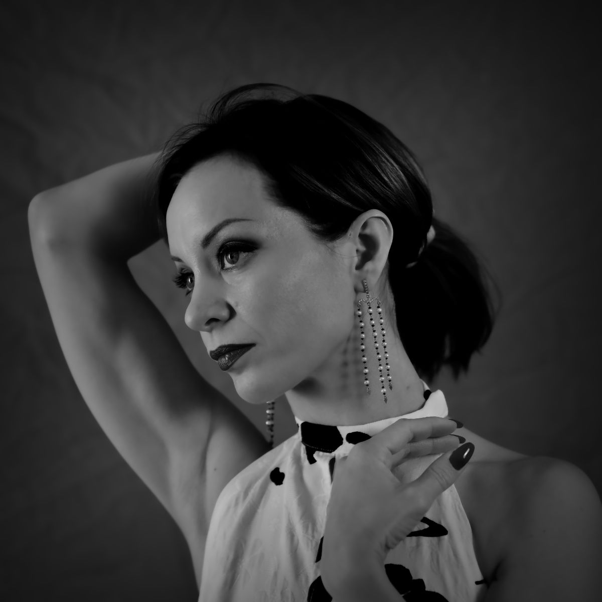 Femme, vêtue d'un haut dos nu, posant avec un bras derrière la tête et l'autre main près du visage ; longues boucles d'oreilles.