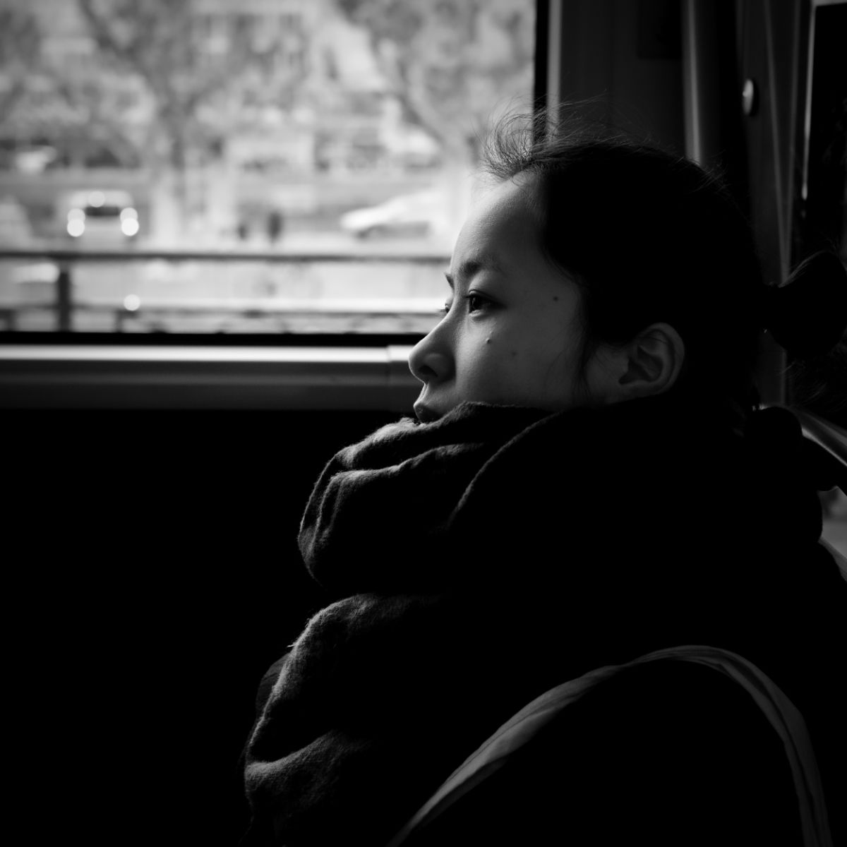 Femme regardant par la fenêtre d'un bus, le menton appuyé sur sa main, en noir et blanc.