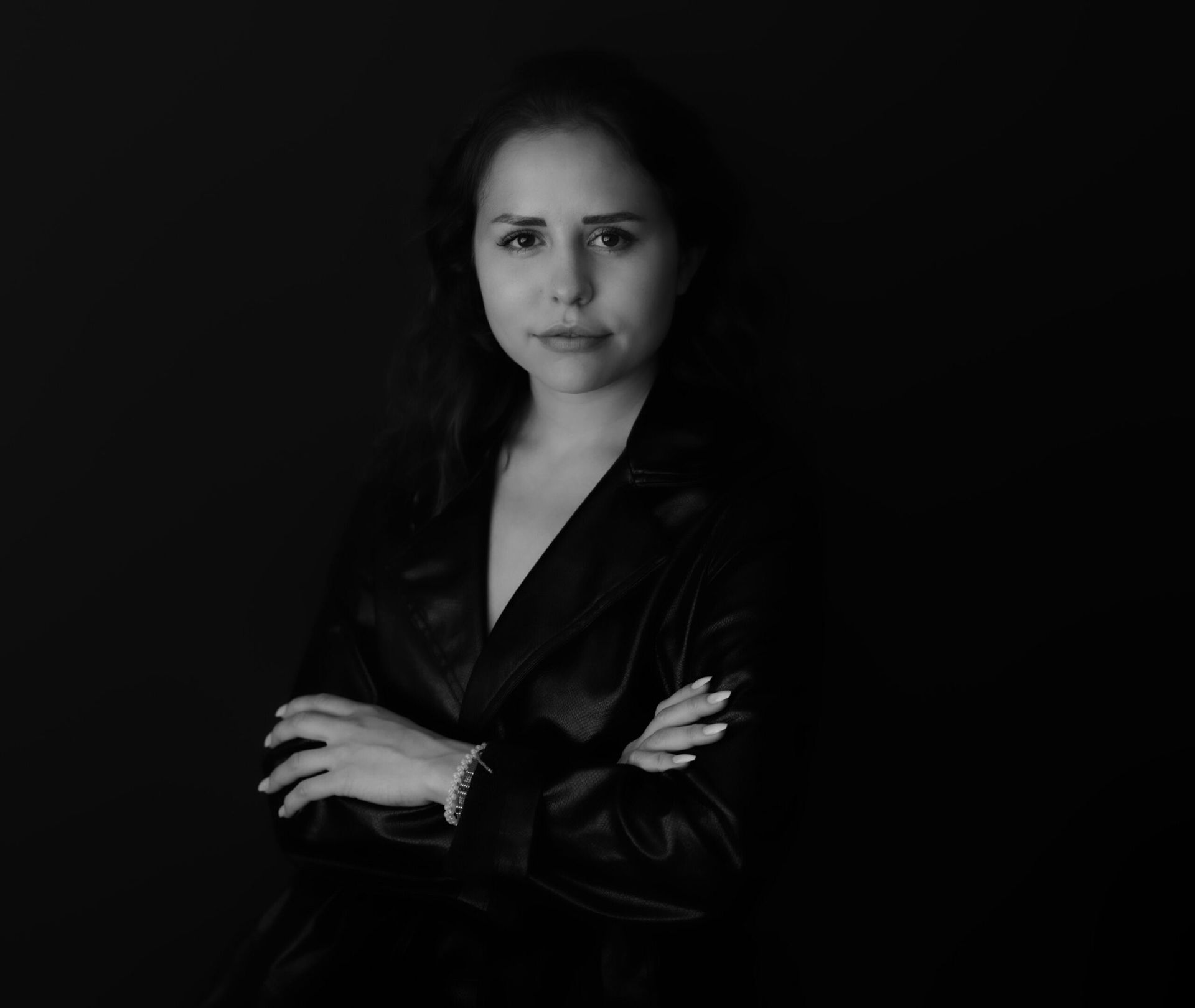 Femme en veste de cuir, les bras croisés, regardant droit devant elle sur un fond sombre.