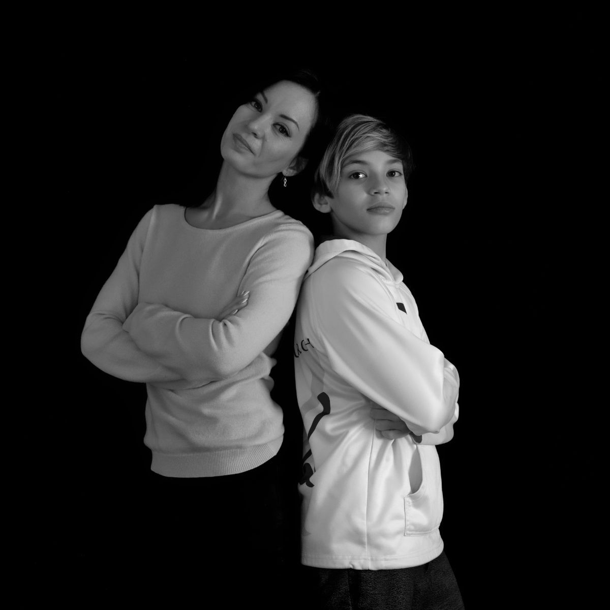 Deux personnes se tiennent dos à dos, les bras croisés, devant un fond noir.