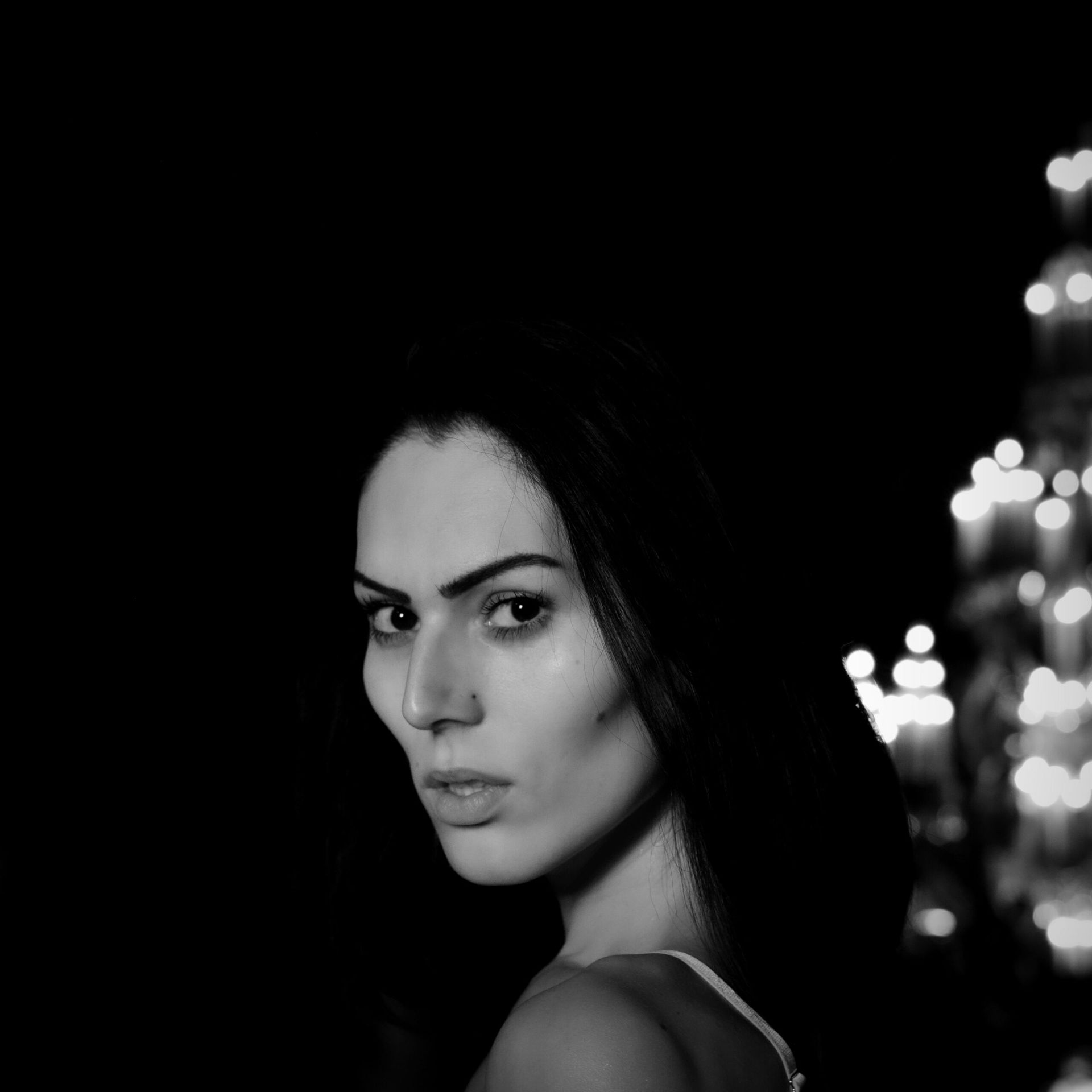 Femme regardant par-dessus son épaule avec une expression inquiète. Fond sombre avec des lumières floues.