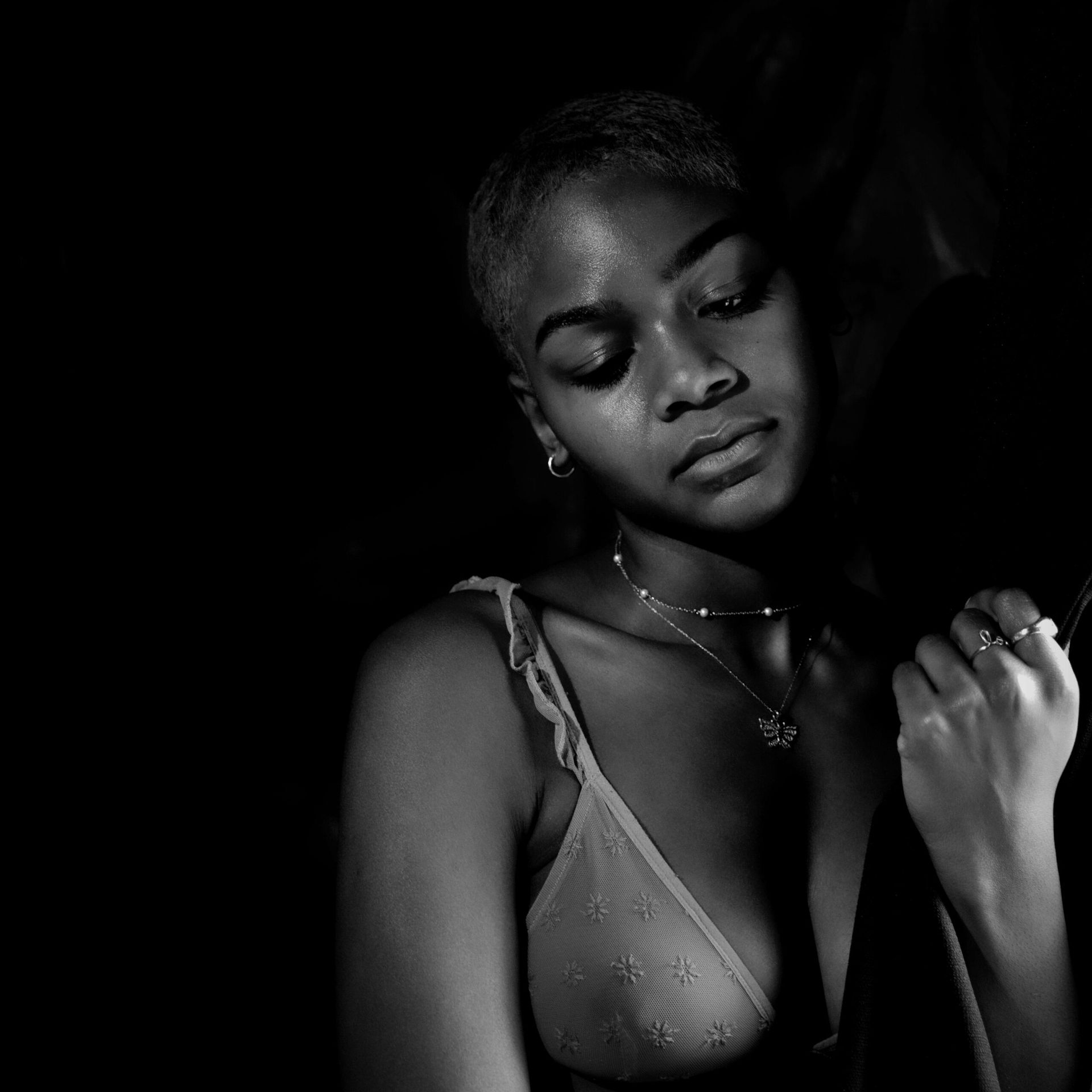 Portrait en noir et blanc d'une personne aux cheveux courts, portant un soutien-gorge et un collier, regardant vers le bas.