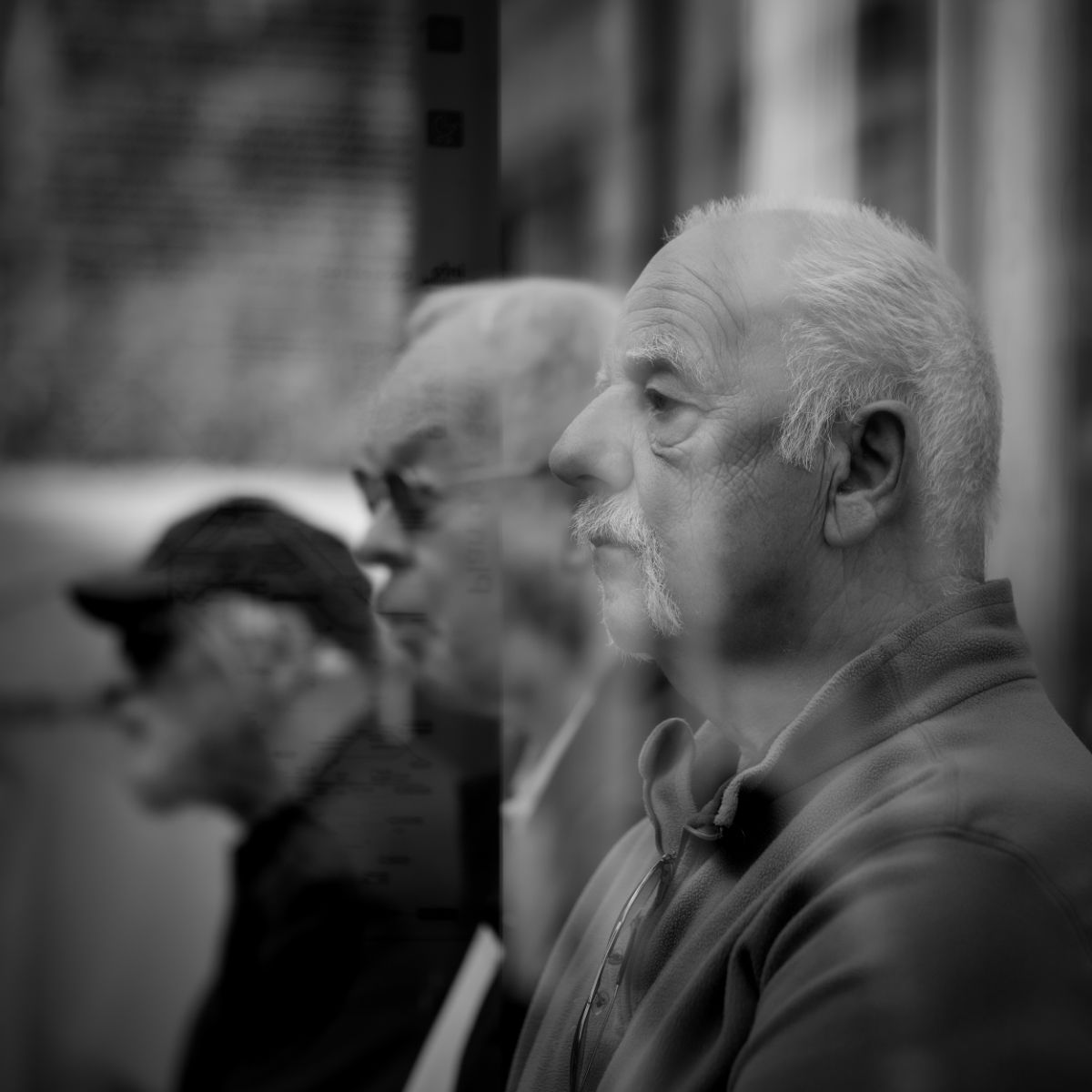 Trois hommes de profil, un au premier plan. Silhouettes floues, en extérieur, en noir et blanc.