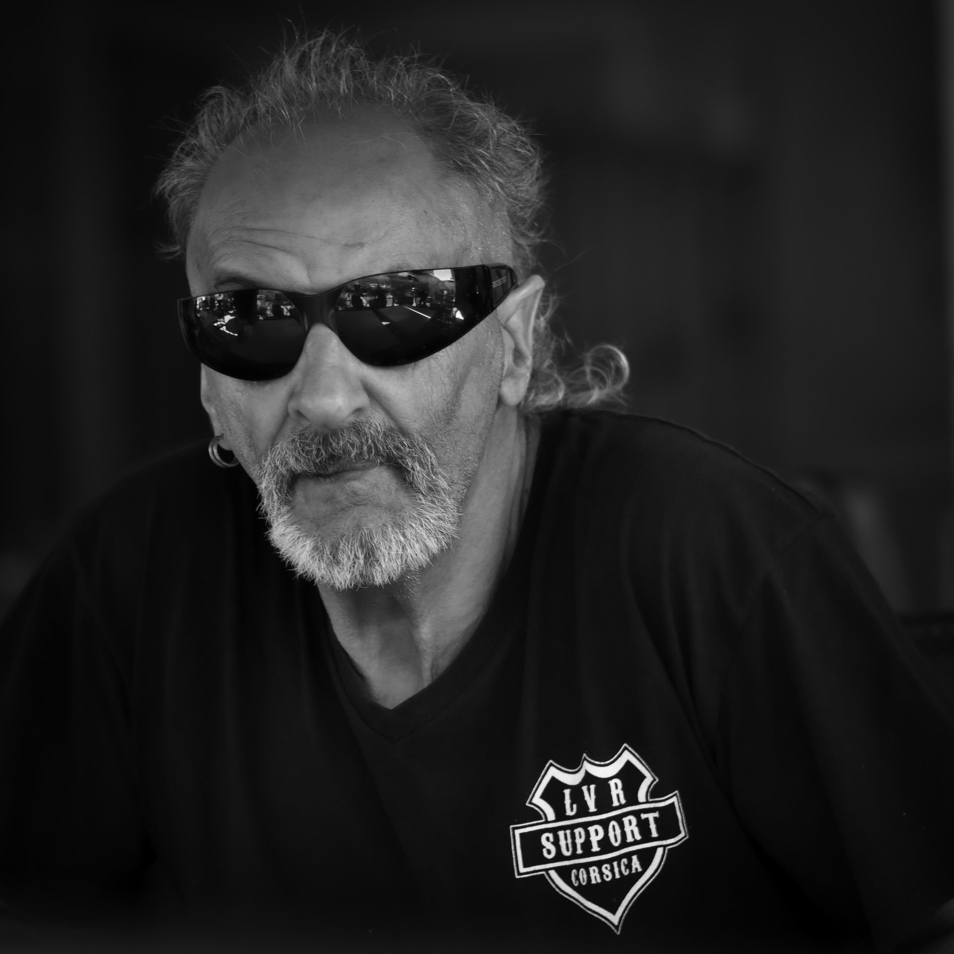 Un homme portant des lunettes de soleil et un bouc, vêtu d'un t-shirt sur lequel on peut lire « LVB Support Motilla ».