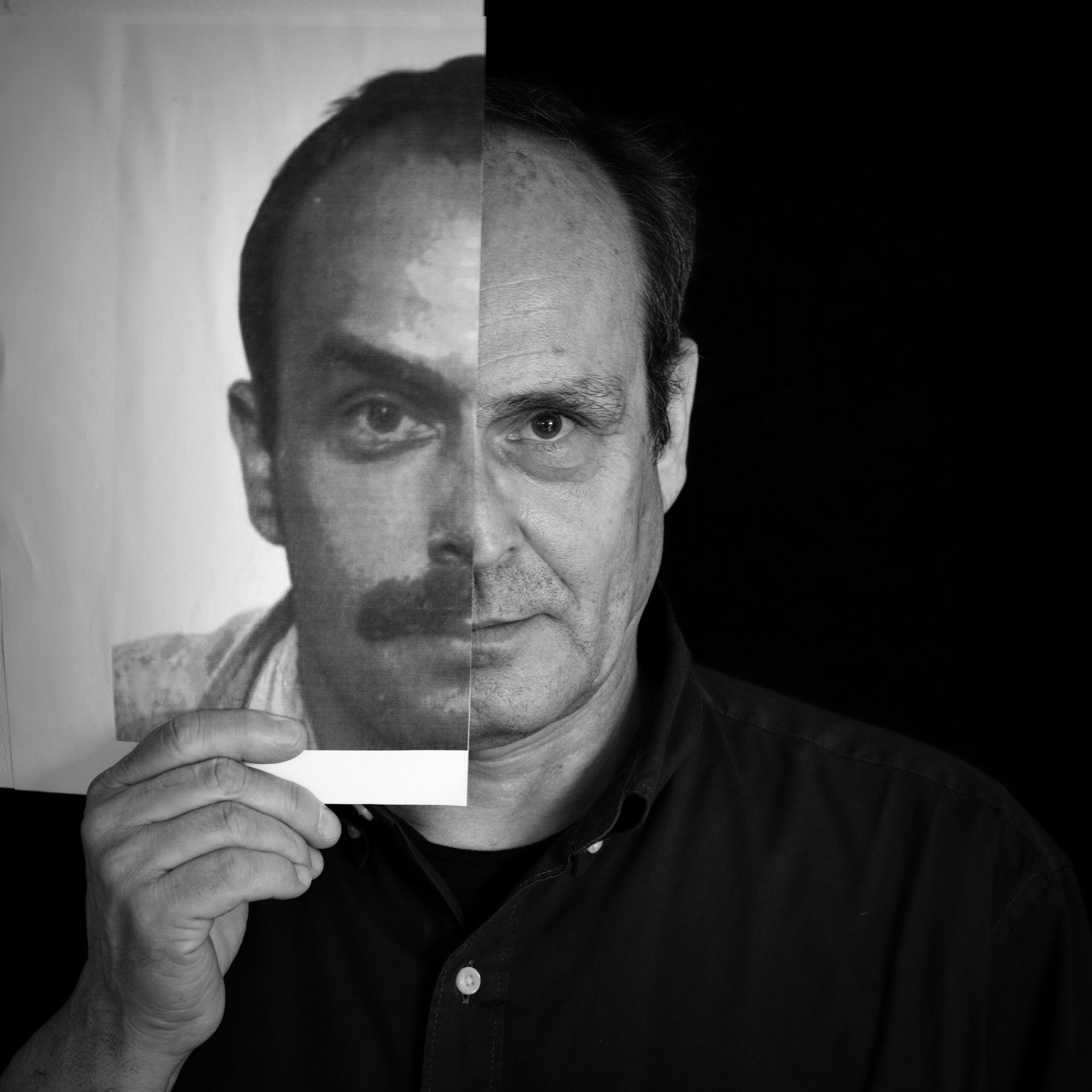 Un homme tient une photo qui recouvre la moitié de son visage ; en noir et blanc.