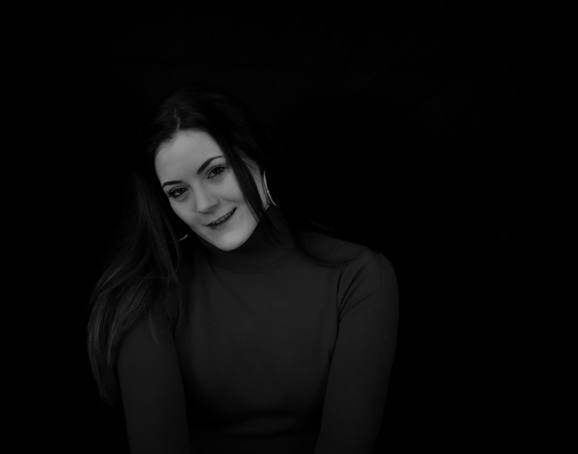 Femme en col roulé souriante, pose de biais, fond sombre.