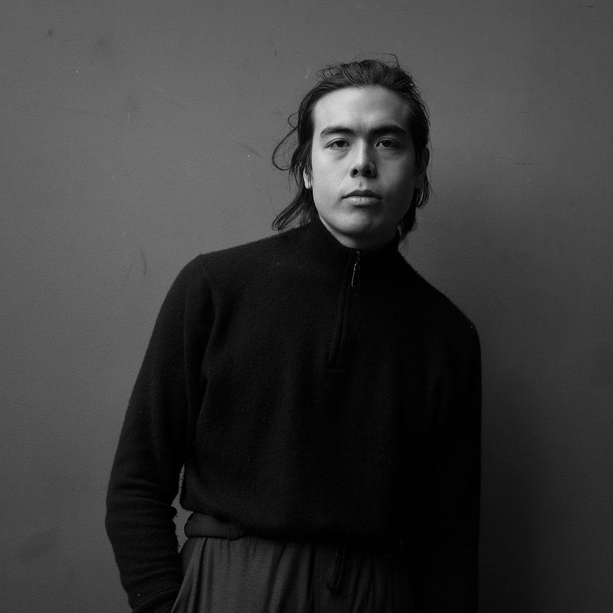 Homme en pull noir, regardant l'objectif, sur fond gris.