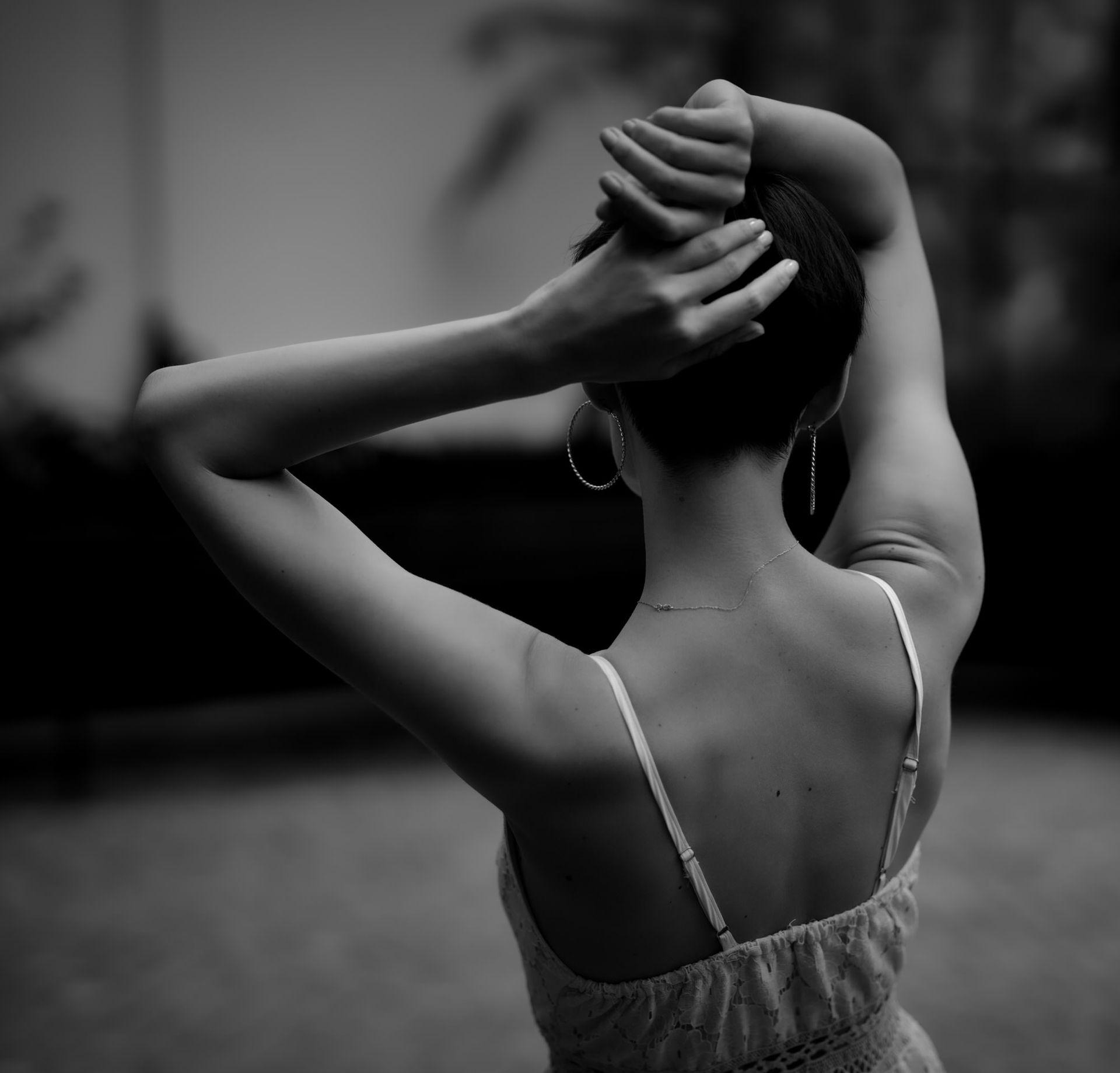 Femme les bras levés derrière la tête, vêtue d'un débardeur à fines bretelles, vue de dos.