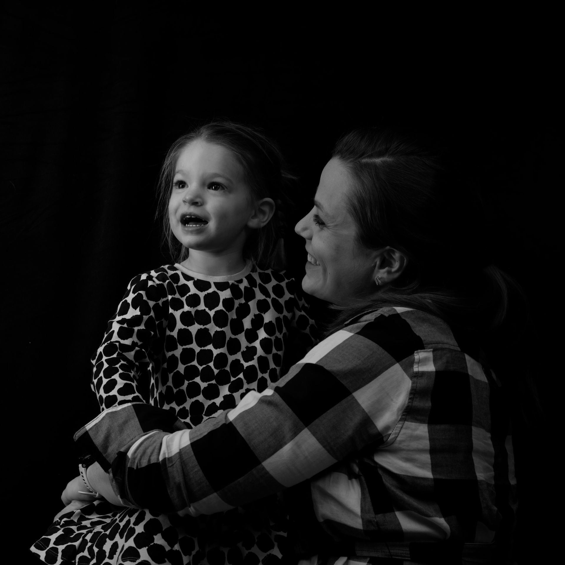 Une femme et un enfant se sourient. L'enfant porte une robe à pois, la femme une robe à carreaux. Noir et blanc.