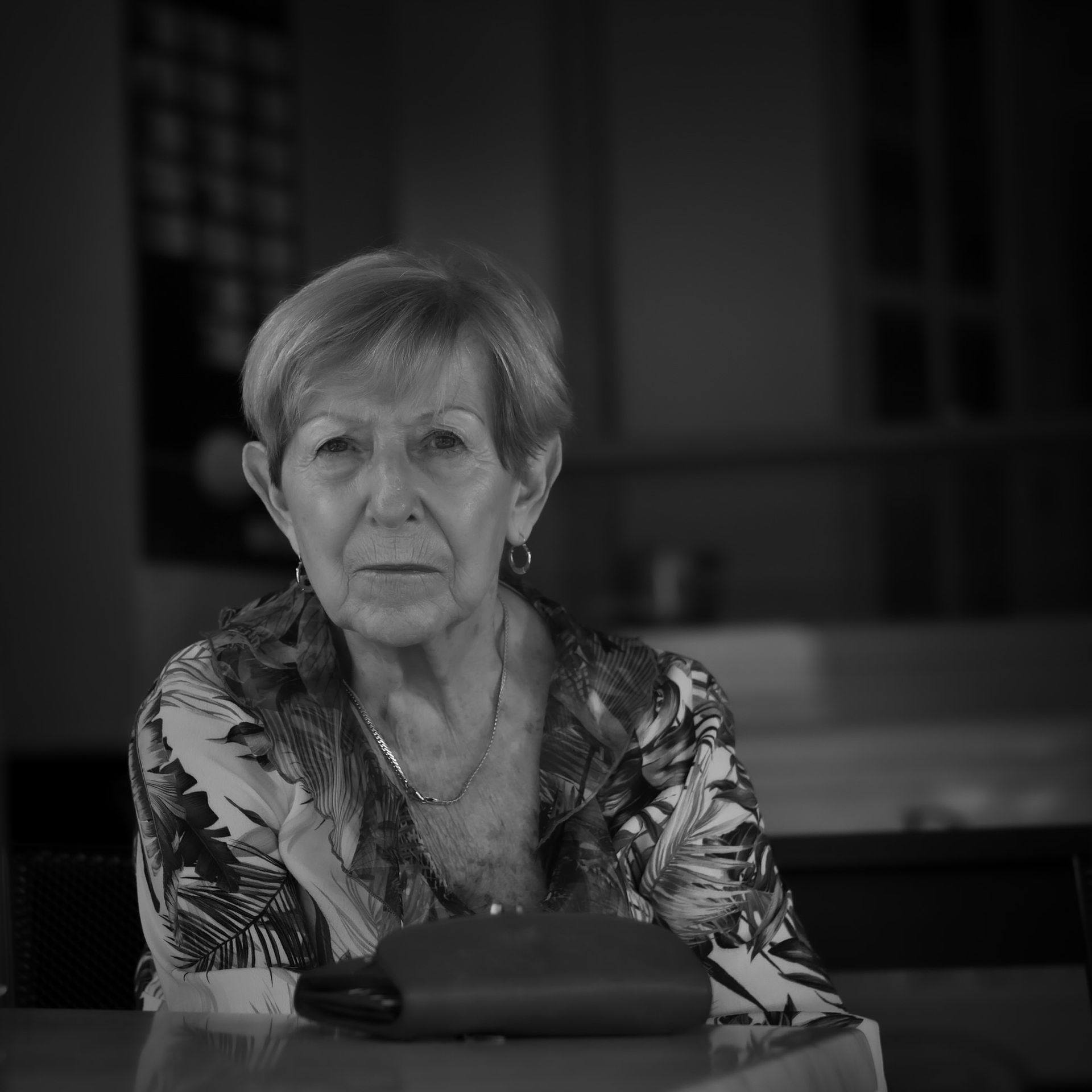 Femme assise à une table, regardant droit devant elle, en noir et blanc.