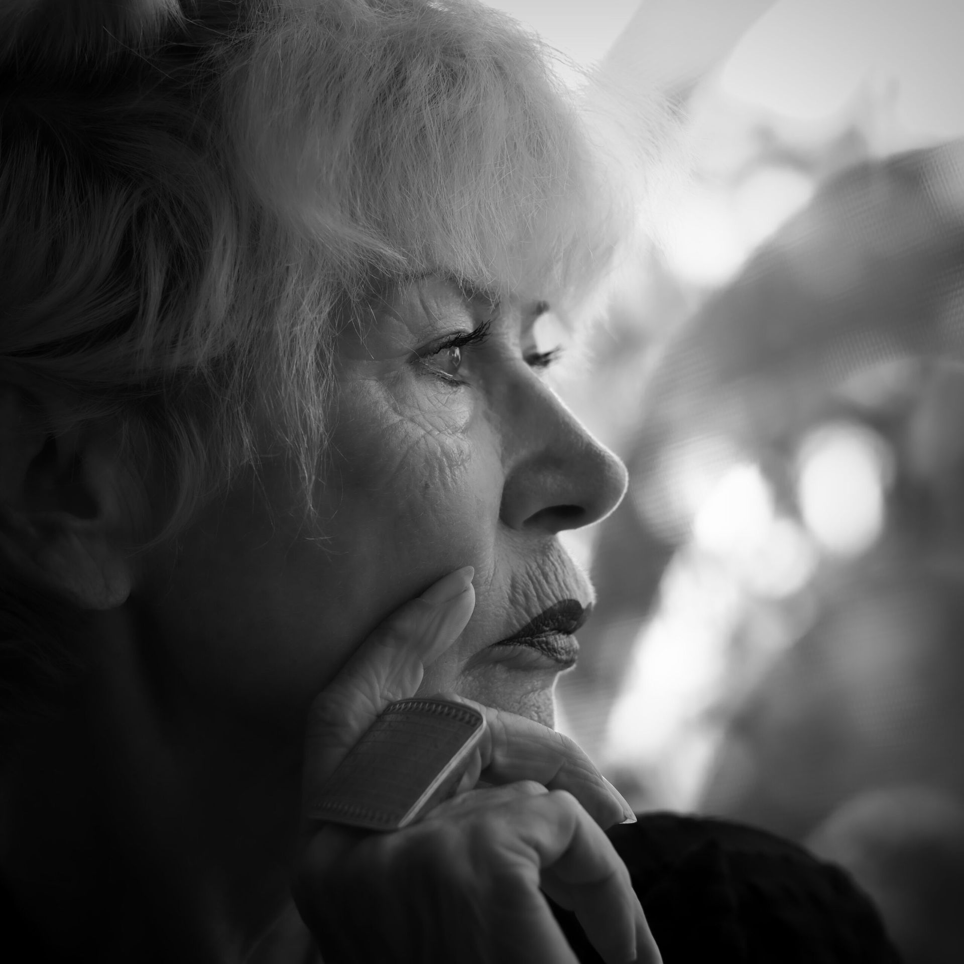 Femme aux cheveux courts et clairs, un doigt sur les lèvres, le regard tourné sur le côté. Portrait en noir et blanc.