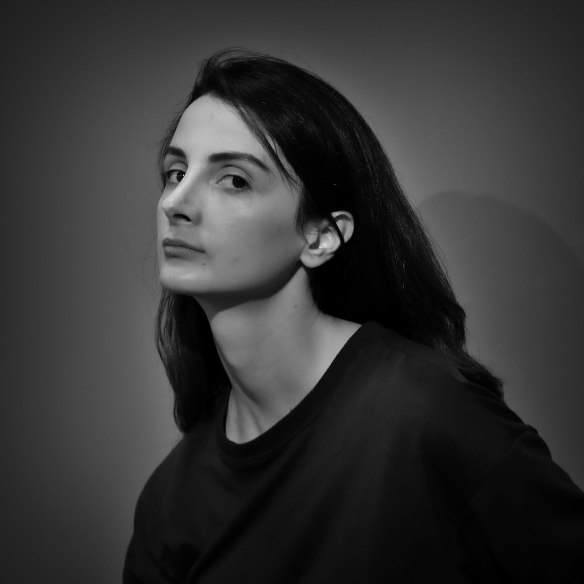 Femme en chemise sombre, regardant par-dessus son épaule avec une expression grave. Photo en noir et blanc.