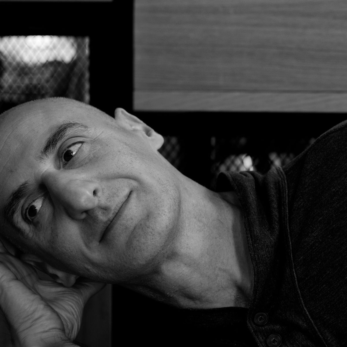 Homme au crâne rasé, penché en avant, regardant hors champ. Photo en noir et blanc.