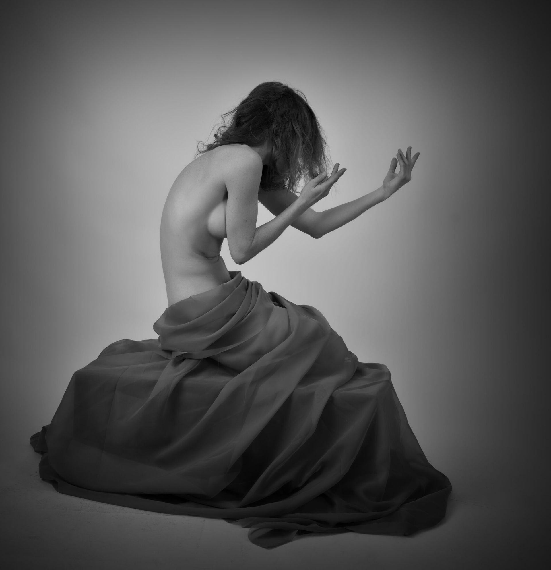 Une personne nue, le dos cambré, assise sur une surface drapée, les bras levés.