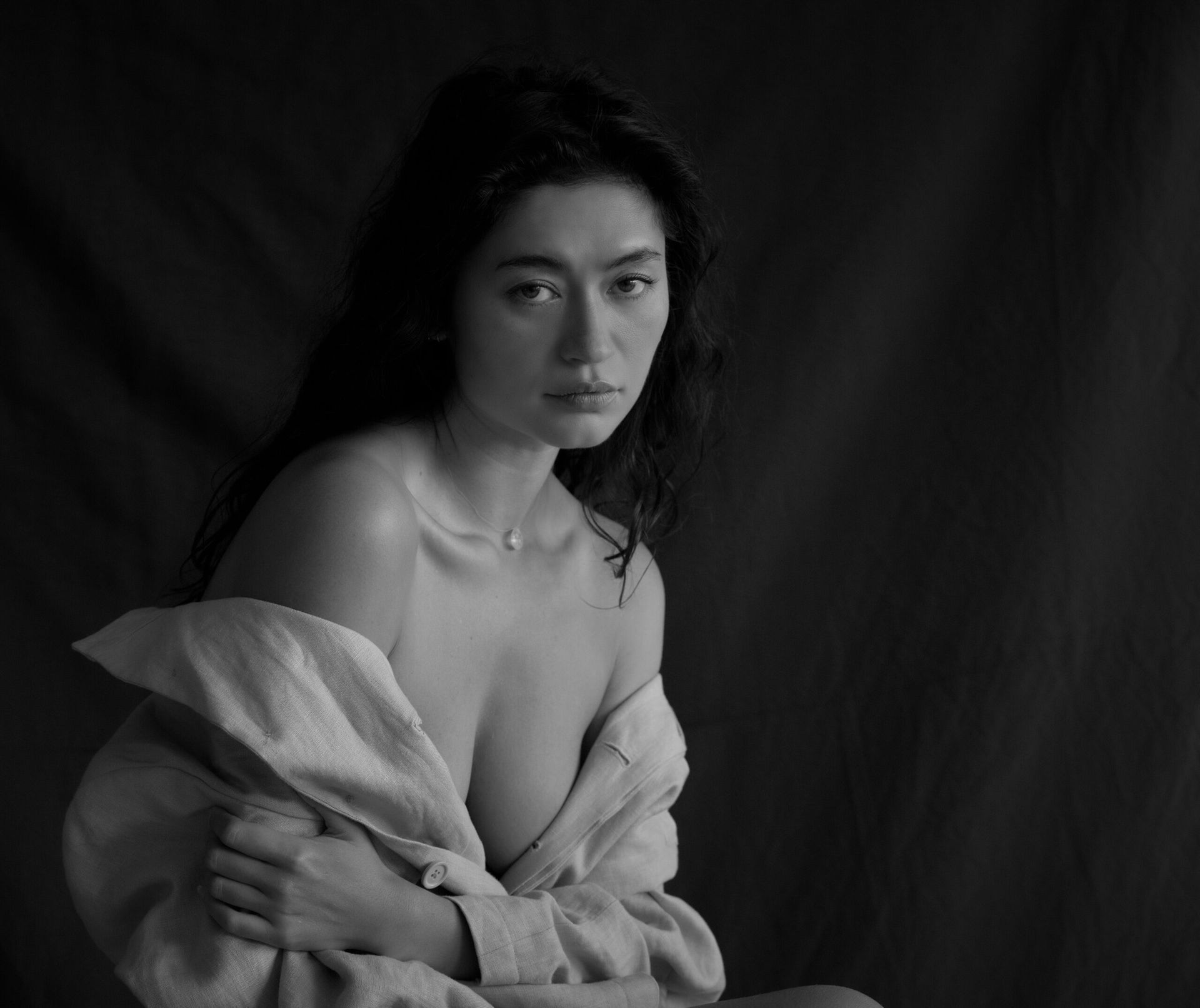 Femme aux longs cheveux noirs, vêtue d'une chemise claire ouverte, regardant droit dans les yeux le spectateur. Noir et blanc.